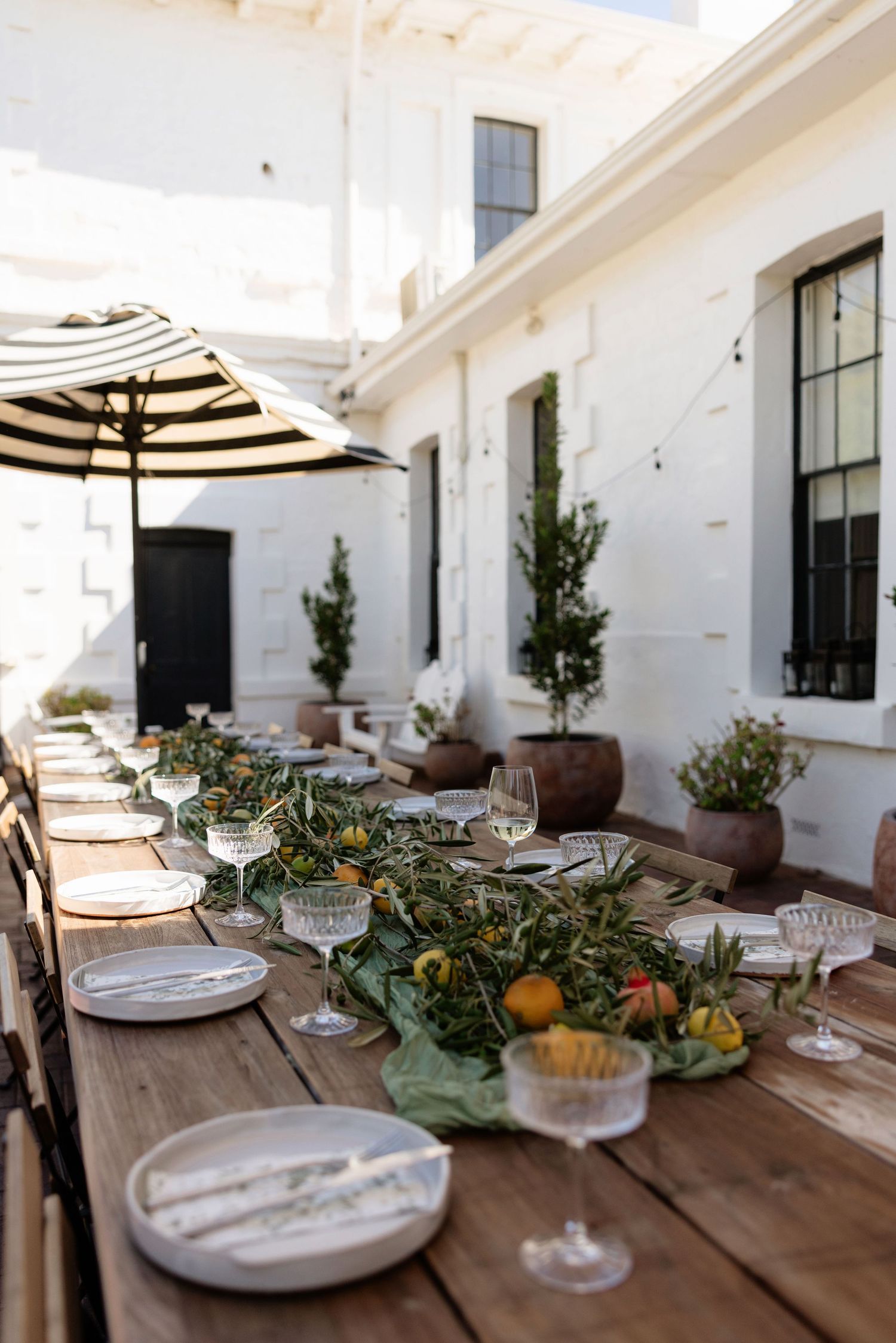 Elegant outdoor wedding reception table with greenery, citrus decor, and striped umbrella.
