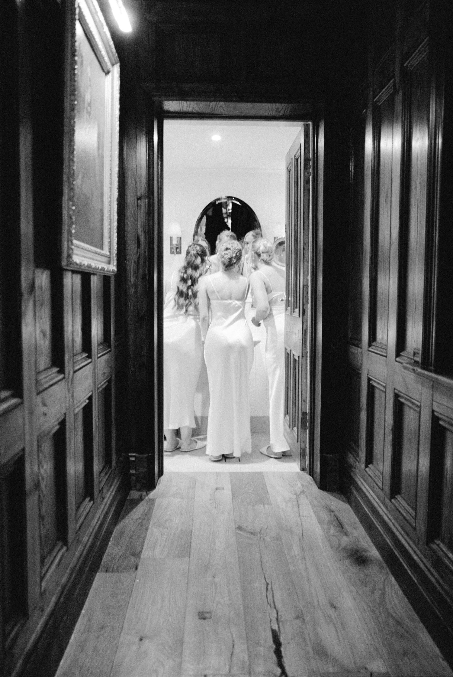 Black and white photo of bridesmaids gathered in a wood-paneled hallway doorway.