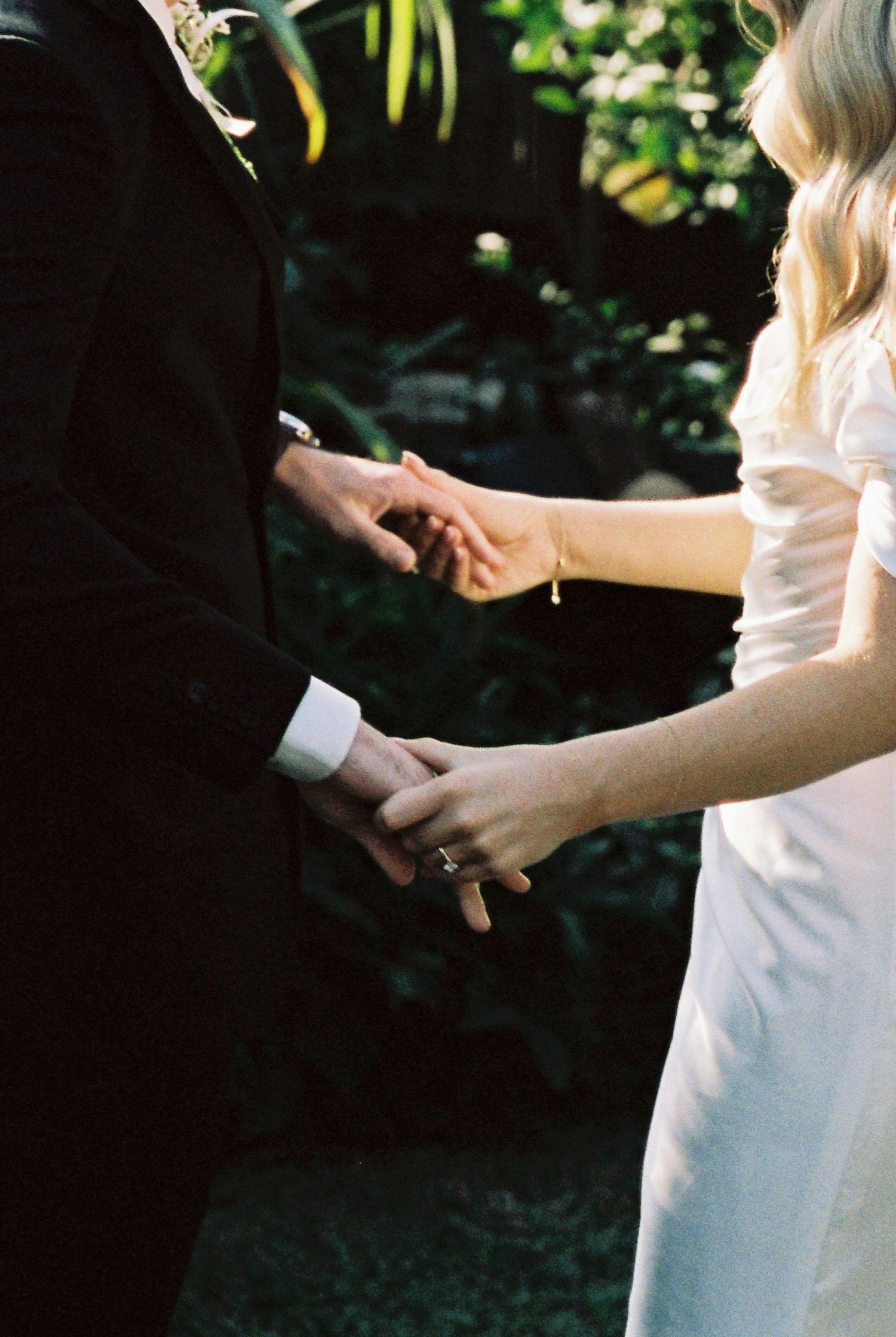Close-up of bride and groom holding hands during outdoor wedding ceremony in lush garden.
