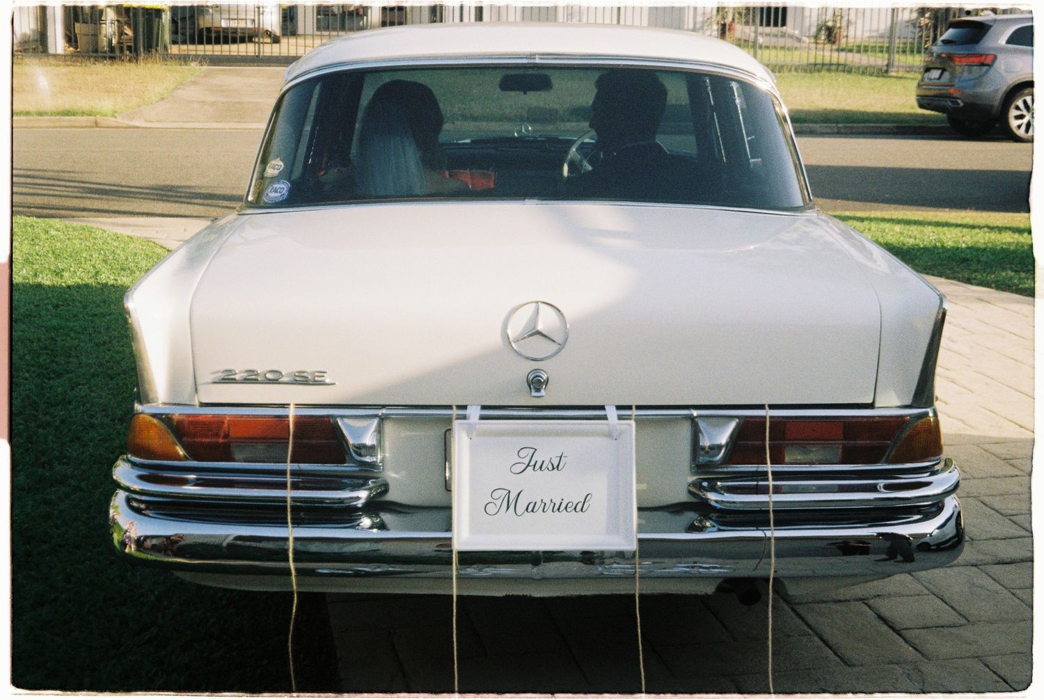 Vintage white Mercedes-Benz with Just Married sign parked on street.