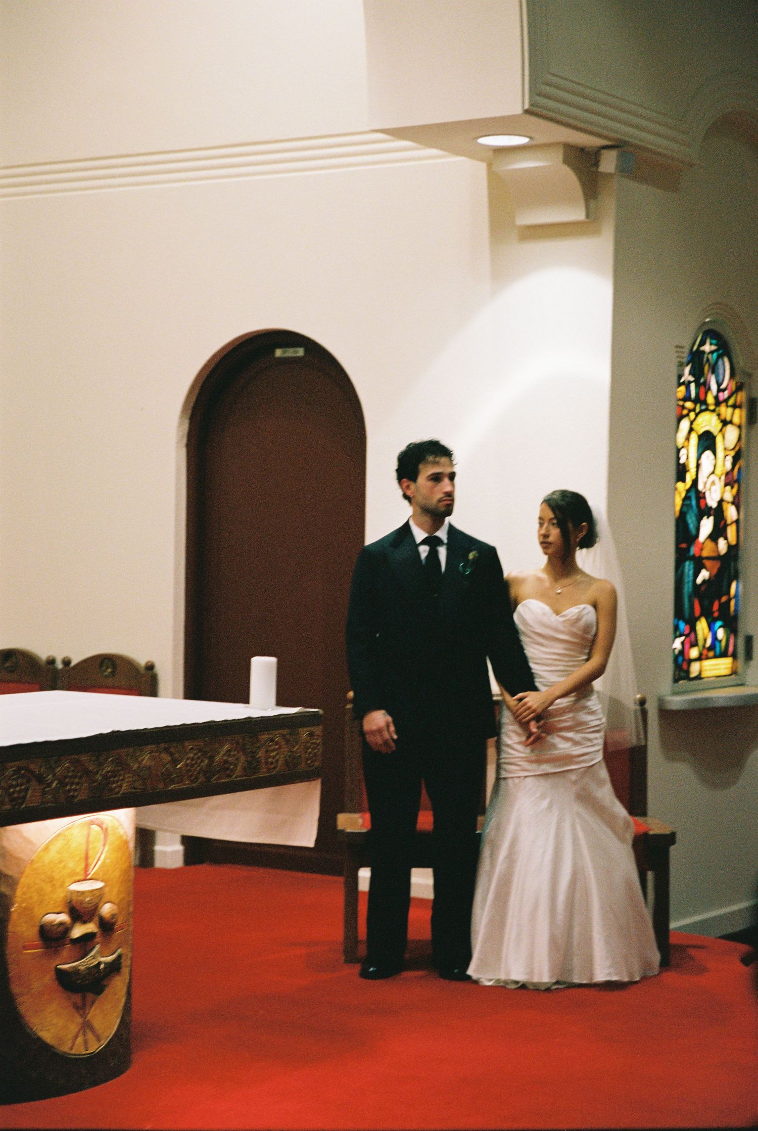 Bride and groom stand at church altar during wedding ceremony with stained glass windows.