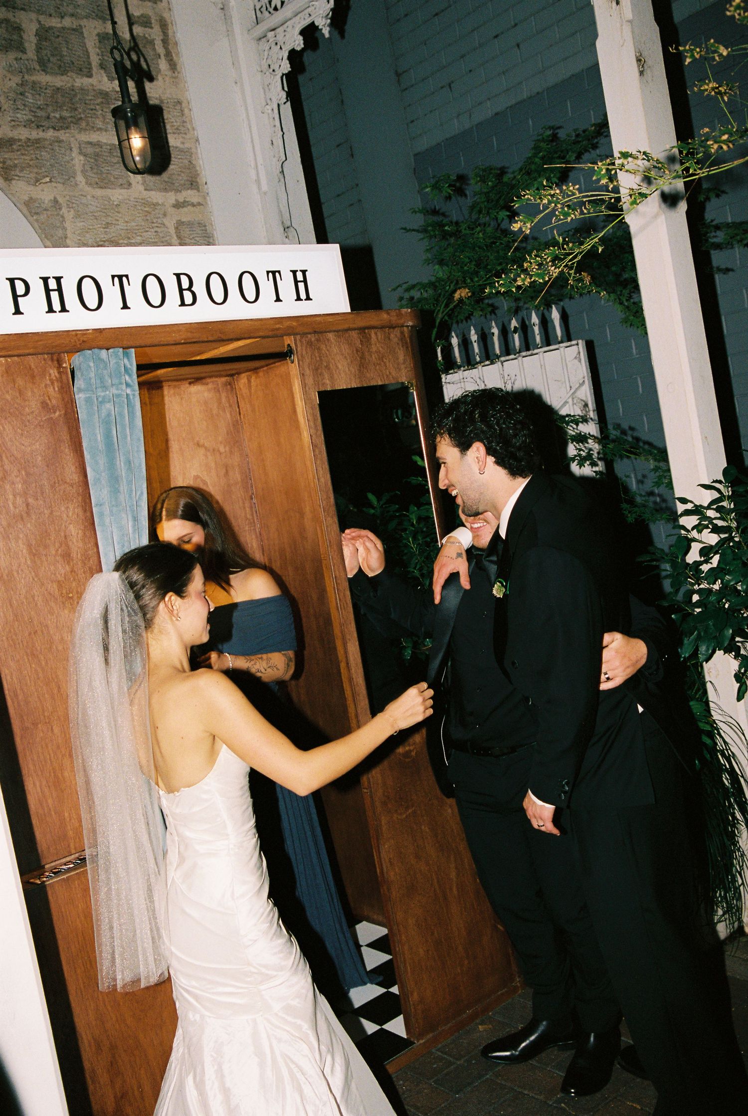 Bride and groom posing at a vintage wooden photobooth at their wedding reception.
