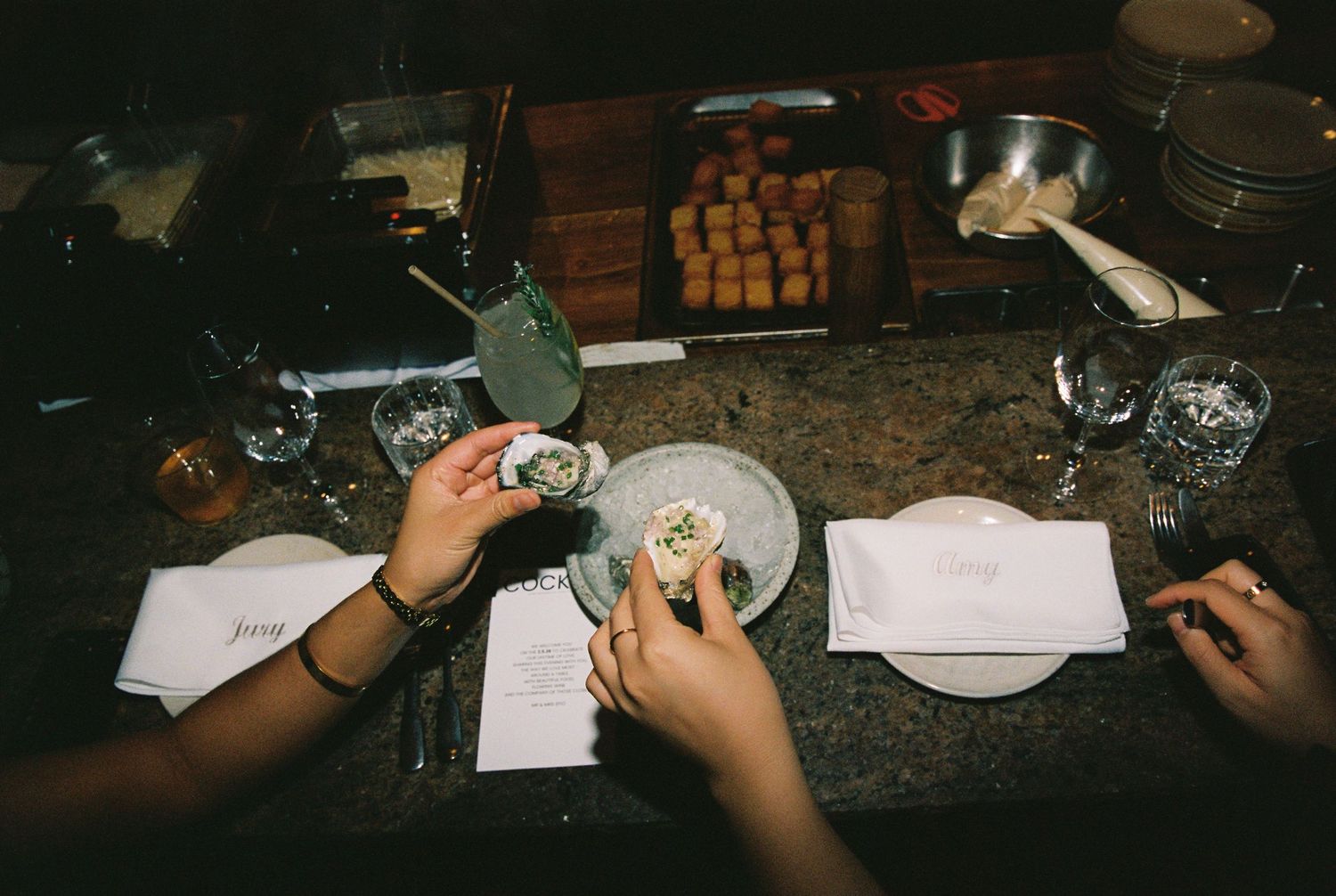 Wedding guests enjoying oysters at elegantly set reception table with menus and glassware.