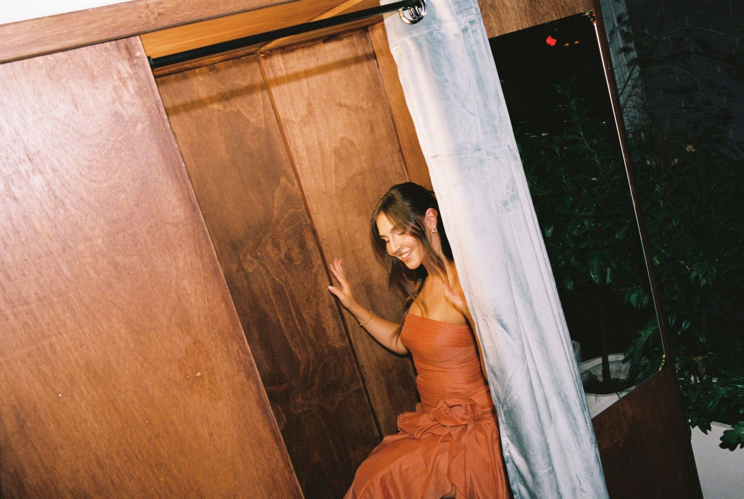 Woman in elegant orange gown stepping out of a wooden photo booth at a wedding event.
