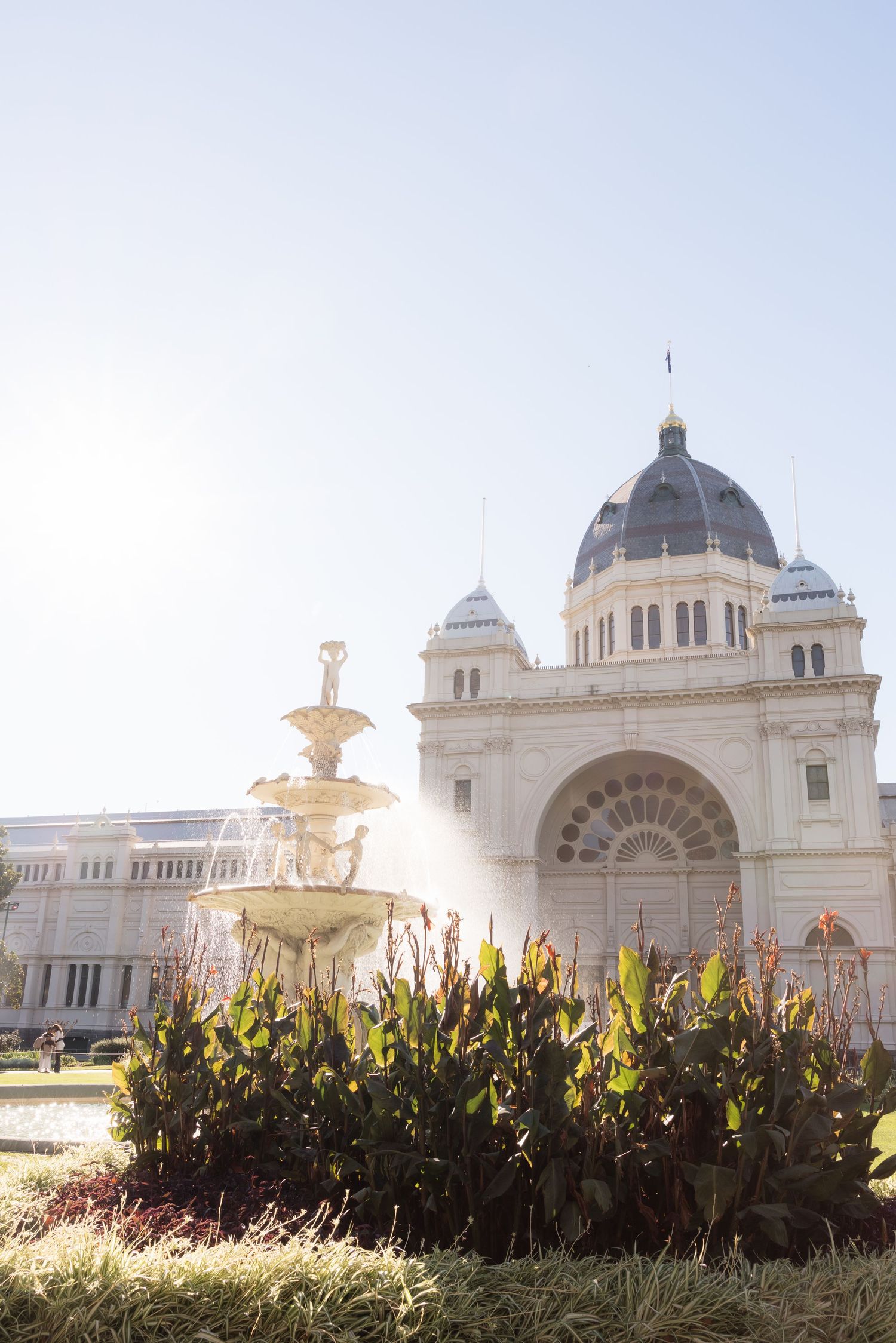 Historic Royal Exhibition Building with ornate fountain and lush gardens in Melbourne, Australia on a sunny day.