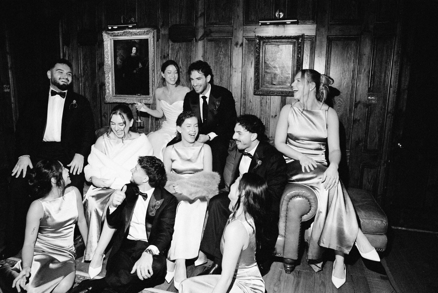 Wedding guests in formal attire relax together in wood-paneled room during elegant reception.
