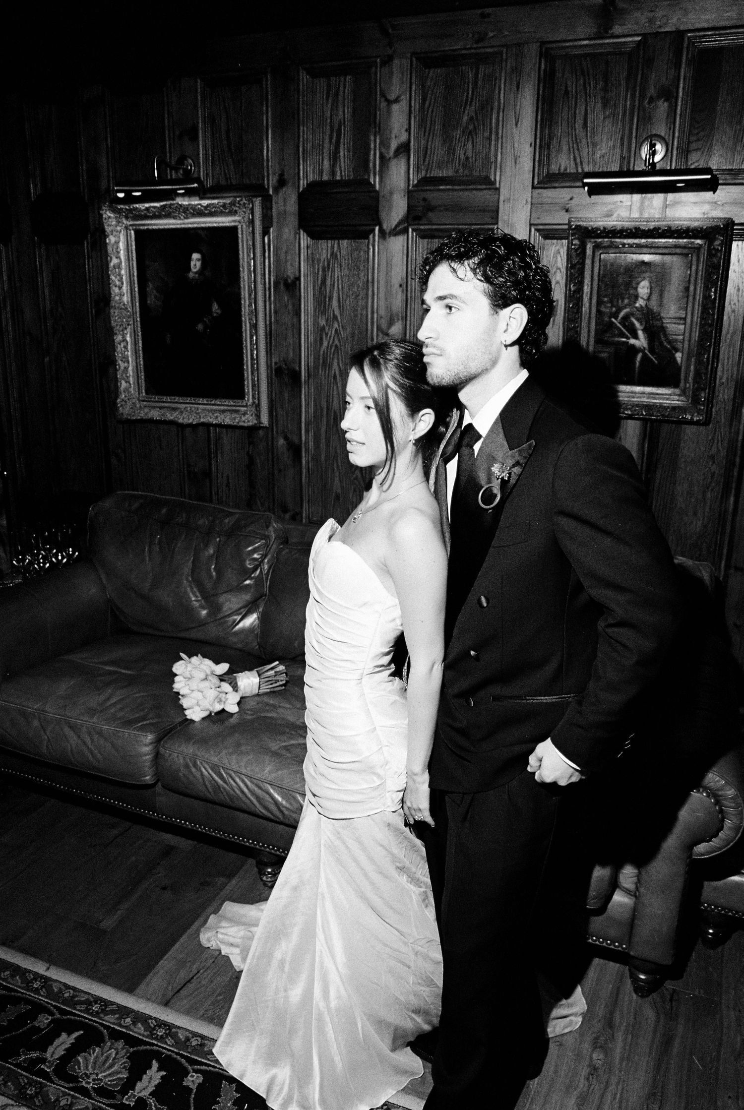 Bride and groom posing together in wood-paneled room with vintage portrait paintings.