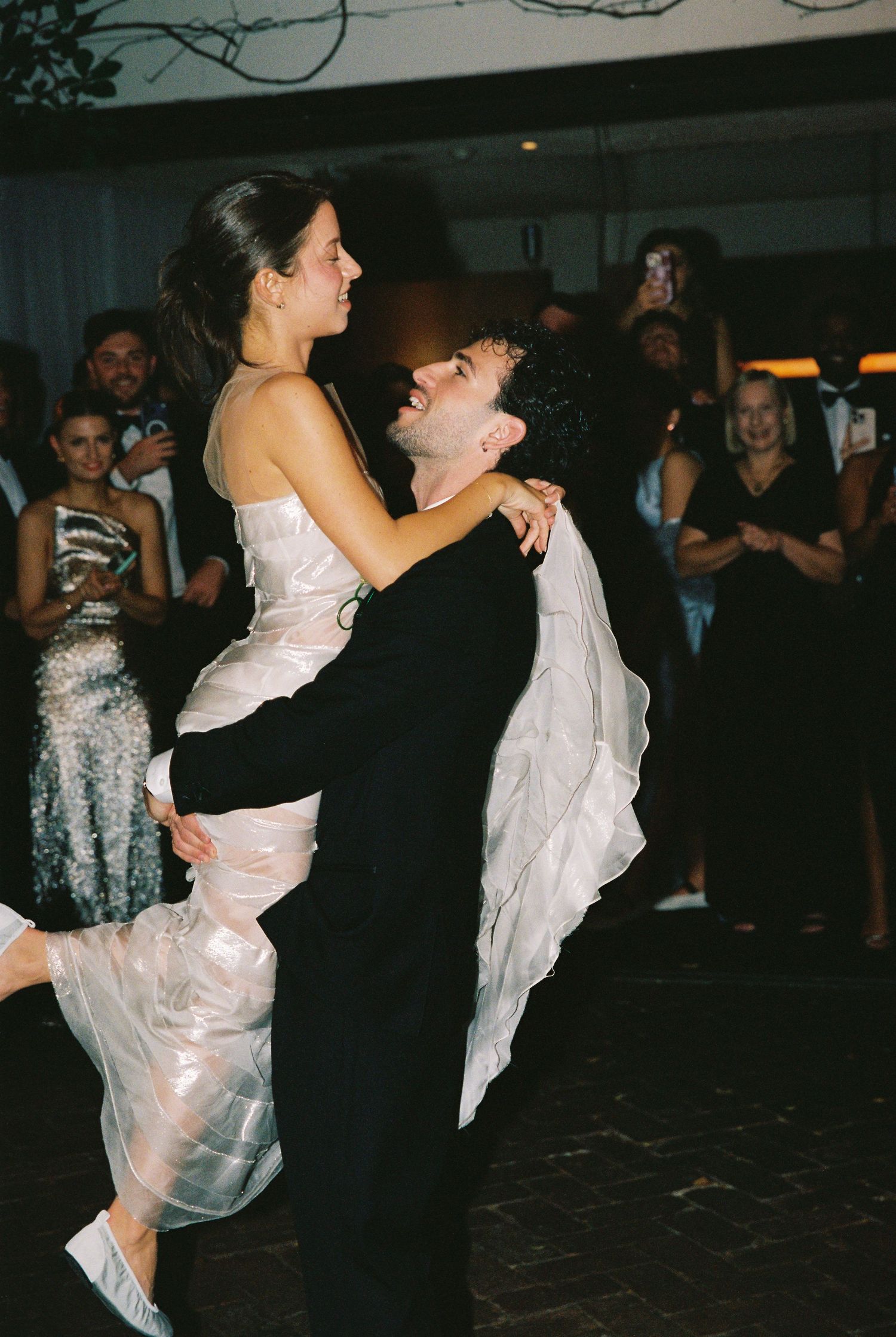 Groom lifting bride during first dance at wedding reception with guests watching.