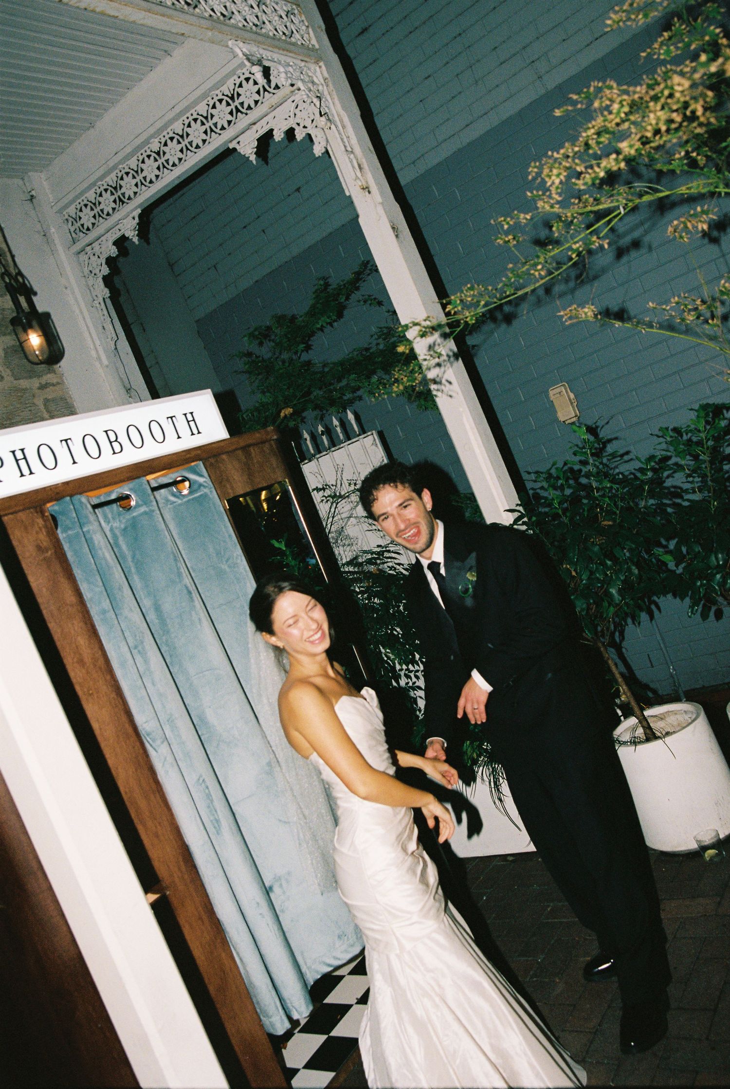Smiling bride and groom pose together outside a wedding reception photobooth.