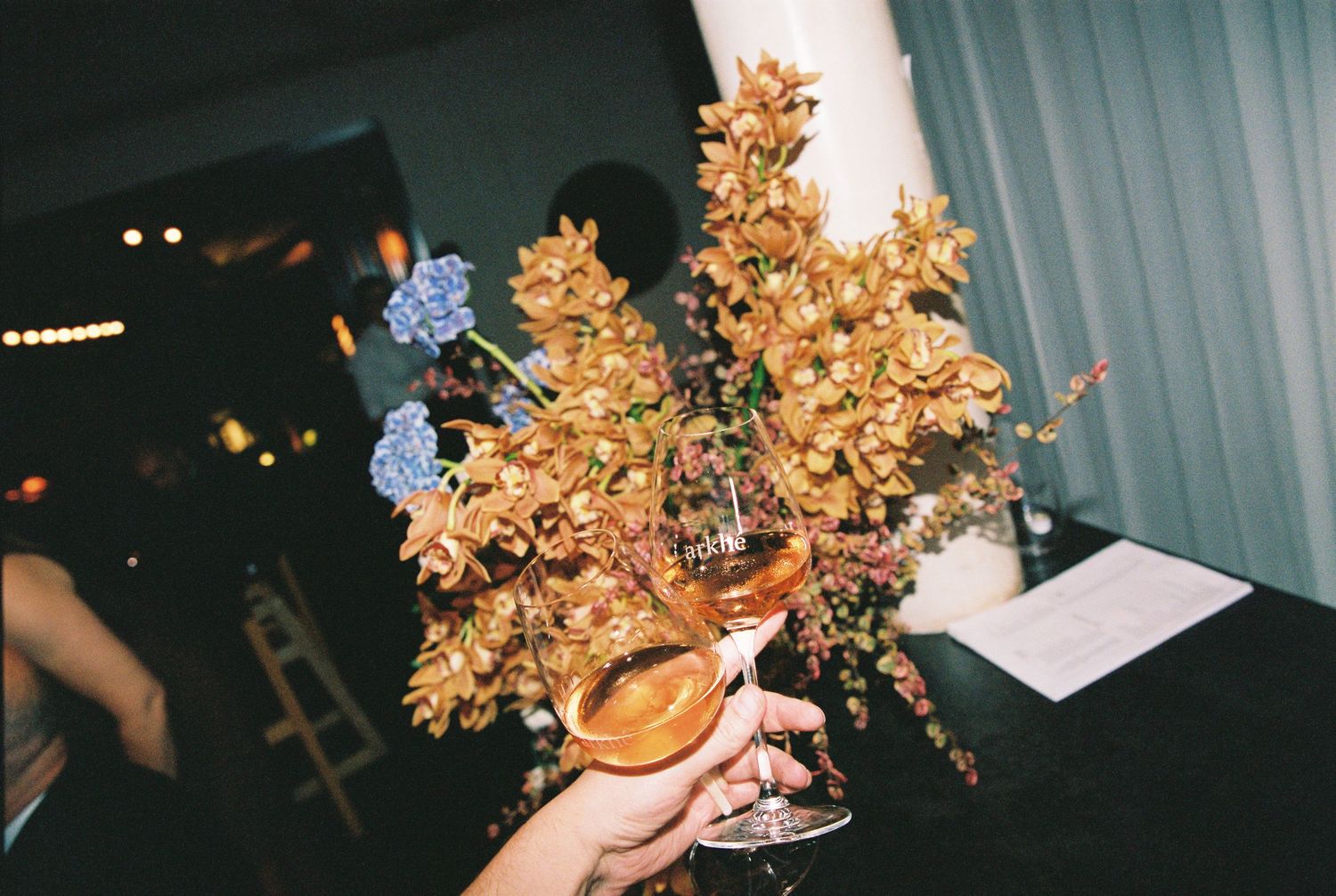 Hand holding a cocktail glass adorned with golden and blue floral arrangement at an elegant wedding reception.