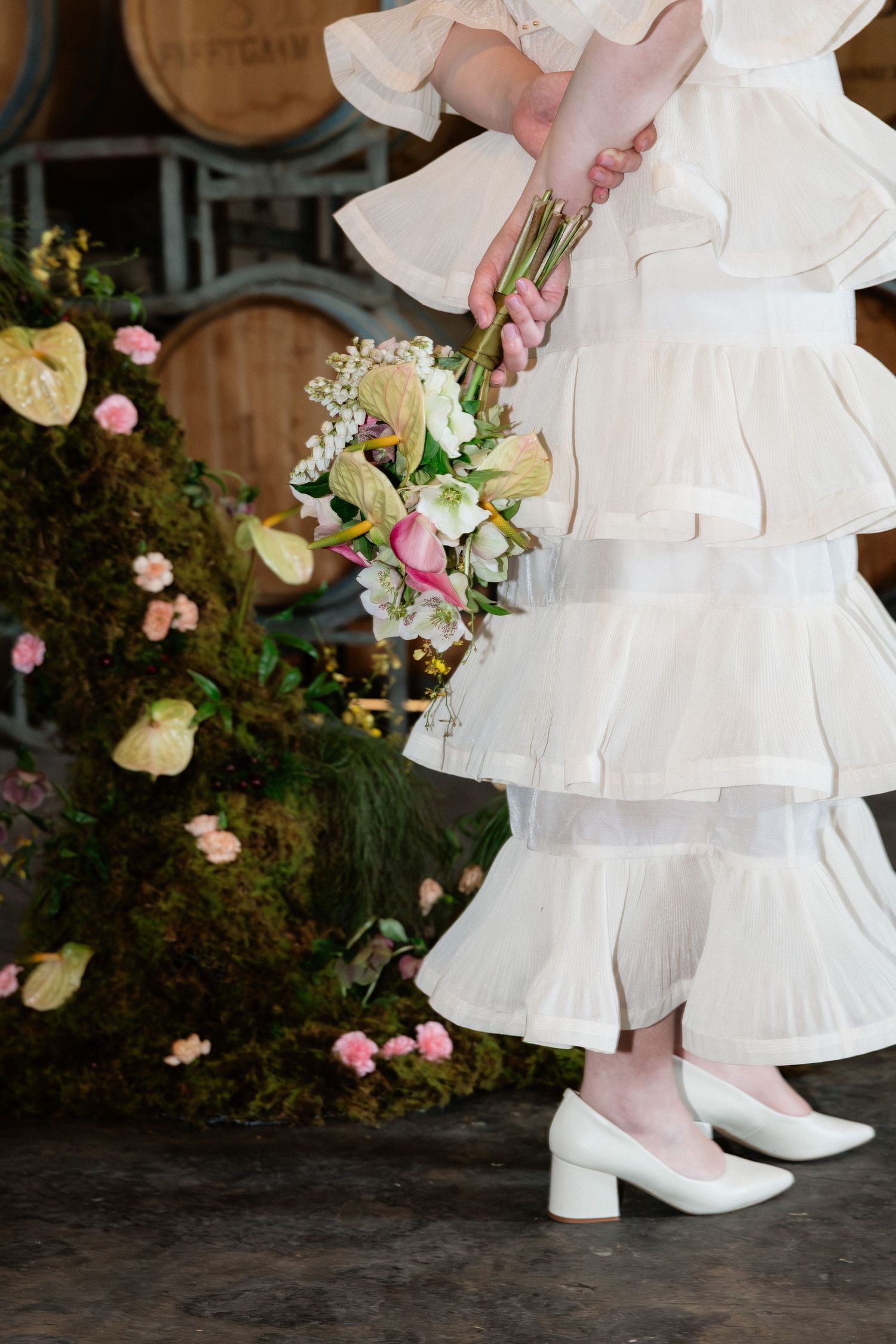 Bride in ruffled white dress holding tropical bouquet with anthurium flowers in winery.