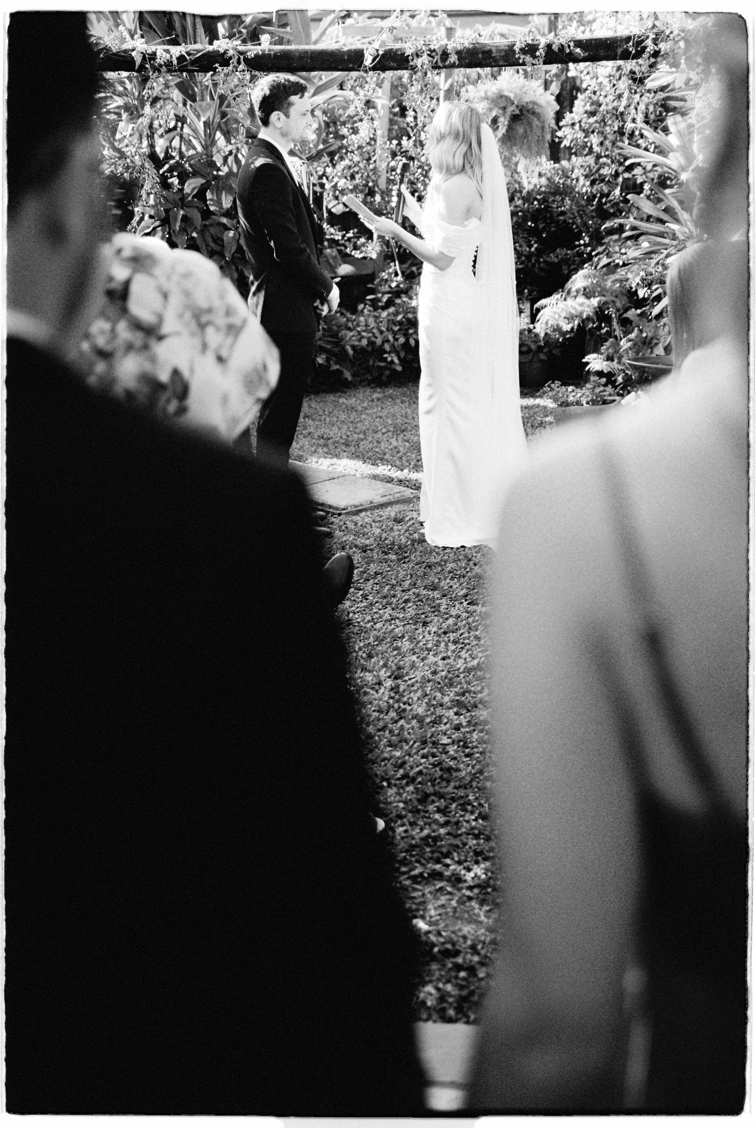 Black and white image of bride and groom exchanging vows at an elegant outdoor garden wedding ceremony.