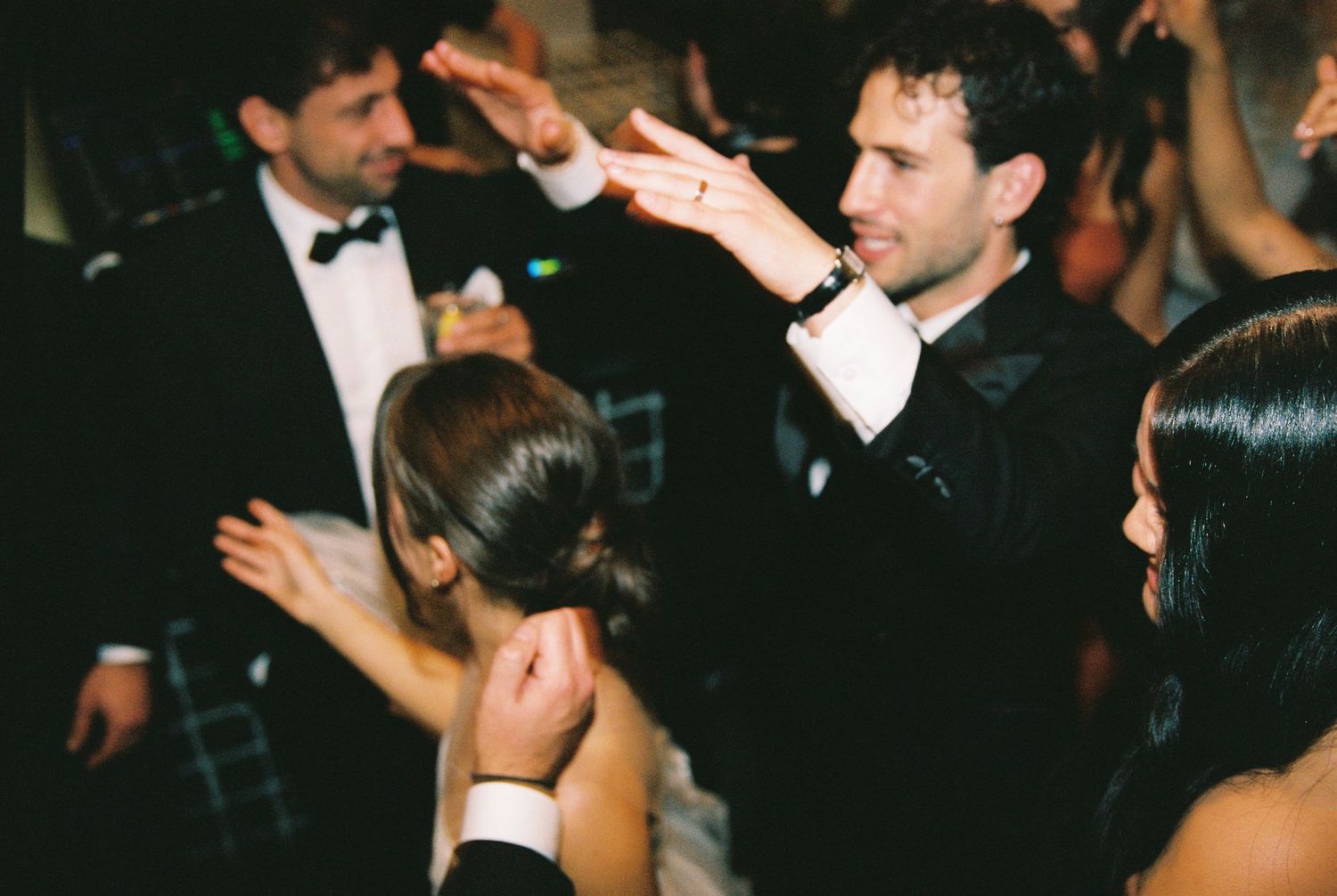 Wedding guest in black tuxedo dances energetically on the reception dance floor.