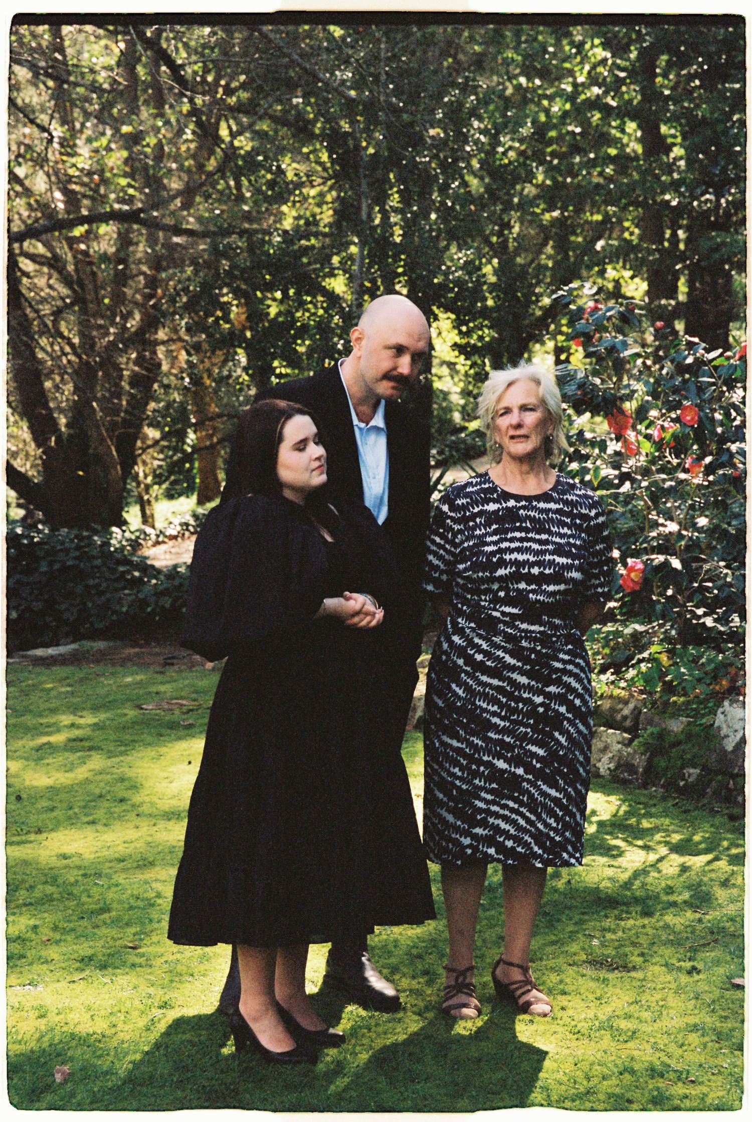 Family portrait of three generations posing in a lush garden with colorful flowers.