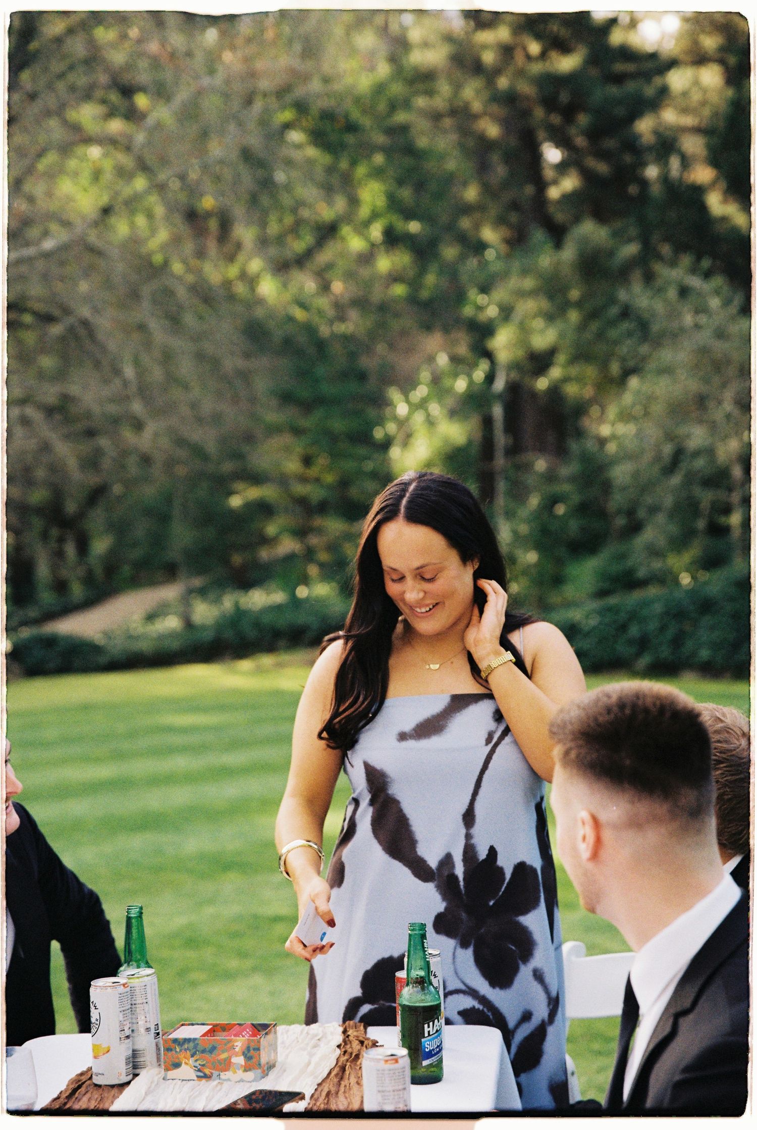 Woman in floral blue dress standing at outdoor wedding reception table on green lawn.
