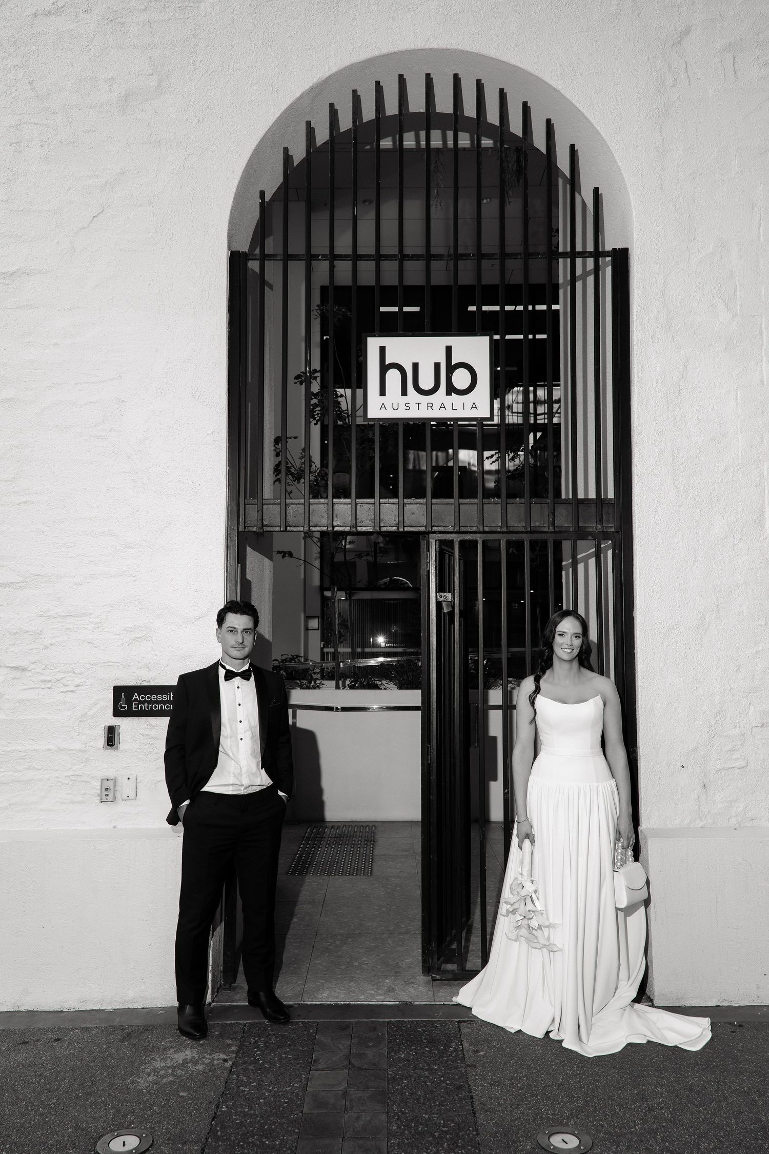Bride and groom pose on either side of an arched entrance to Hub Australia in a black and white portrait.