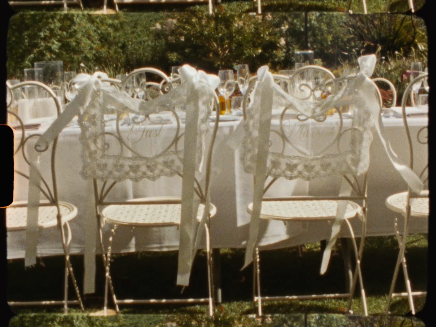Ornate white heart-shaped chairs decorated with white ribbon bows at an outdoor wedding reception table.