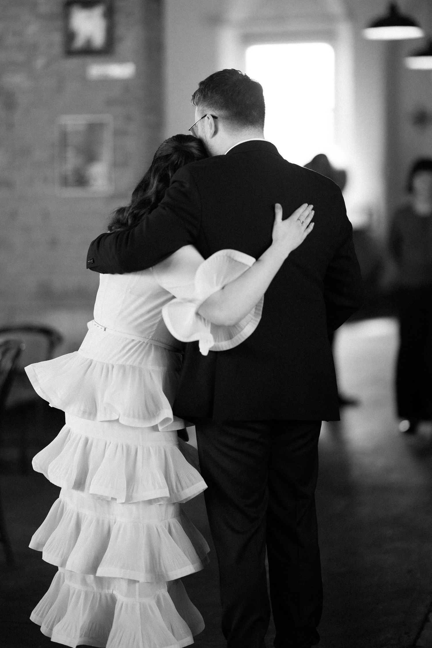 Bride and groom share first dance embrace, bride wearing tiered ruffle wedding dress, black and white wedding photo.