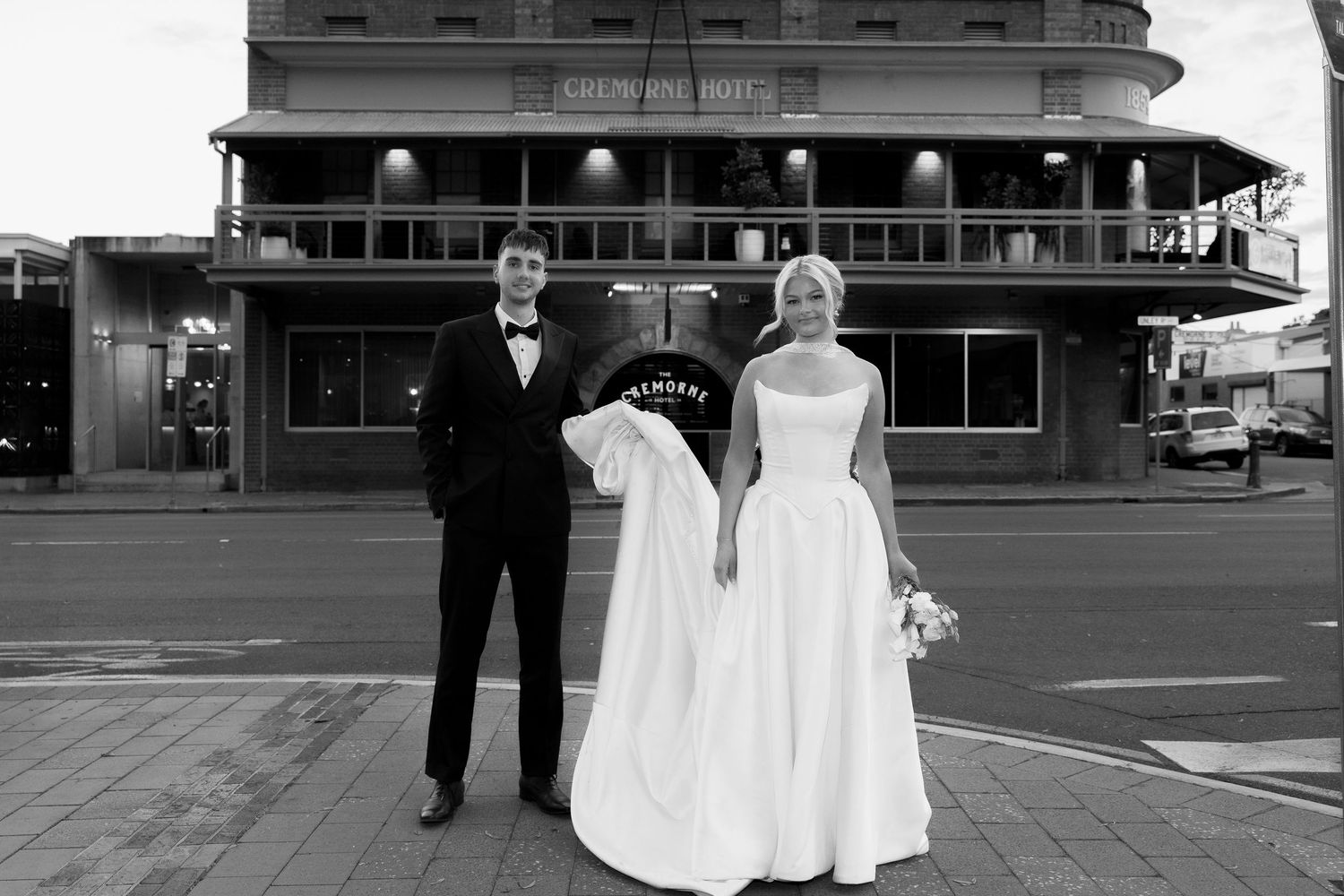 Black and white photo of a bride and groom standing outside a historic building on their wedding day.