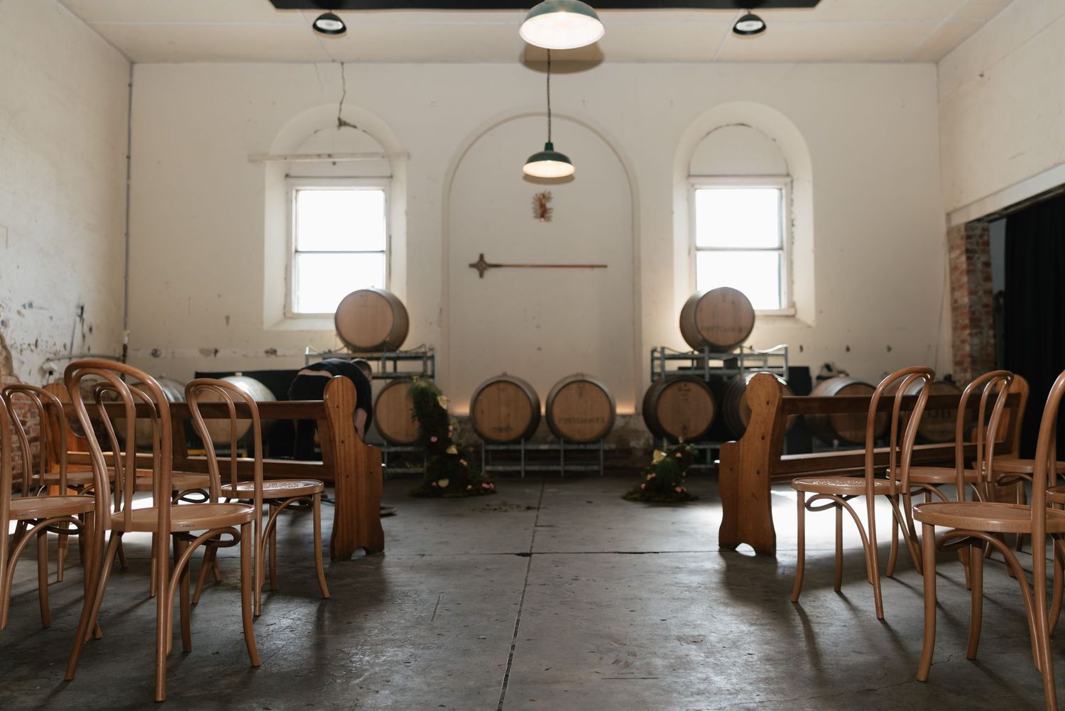 Rustic winery tasting room with wooden barrels, bentwood chairs, and white walls with arched alcove.