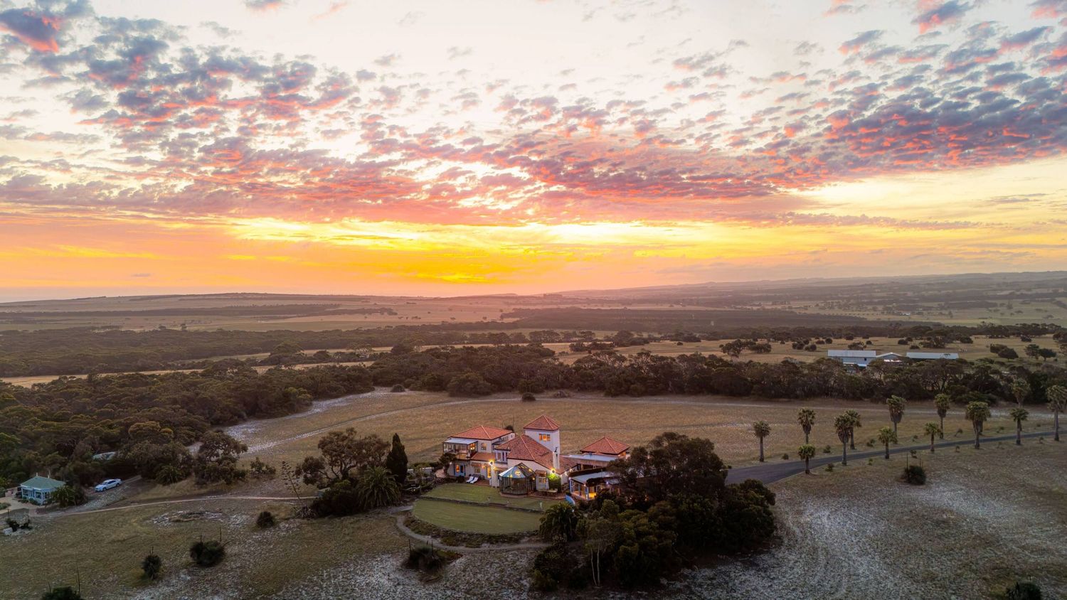 Aerial view of a ranch estate at sunset with vibrant orange and pink skies over vast Texas Hill Country landscape.
