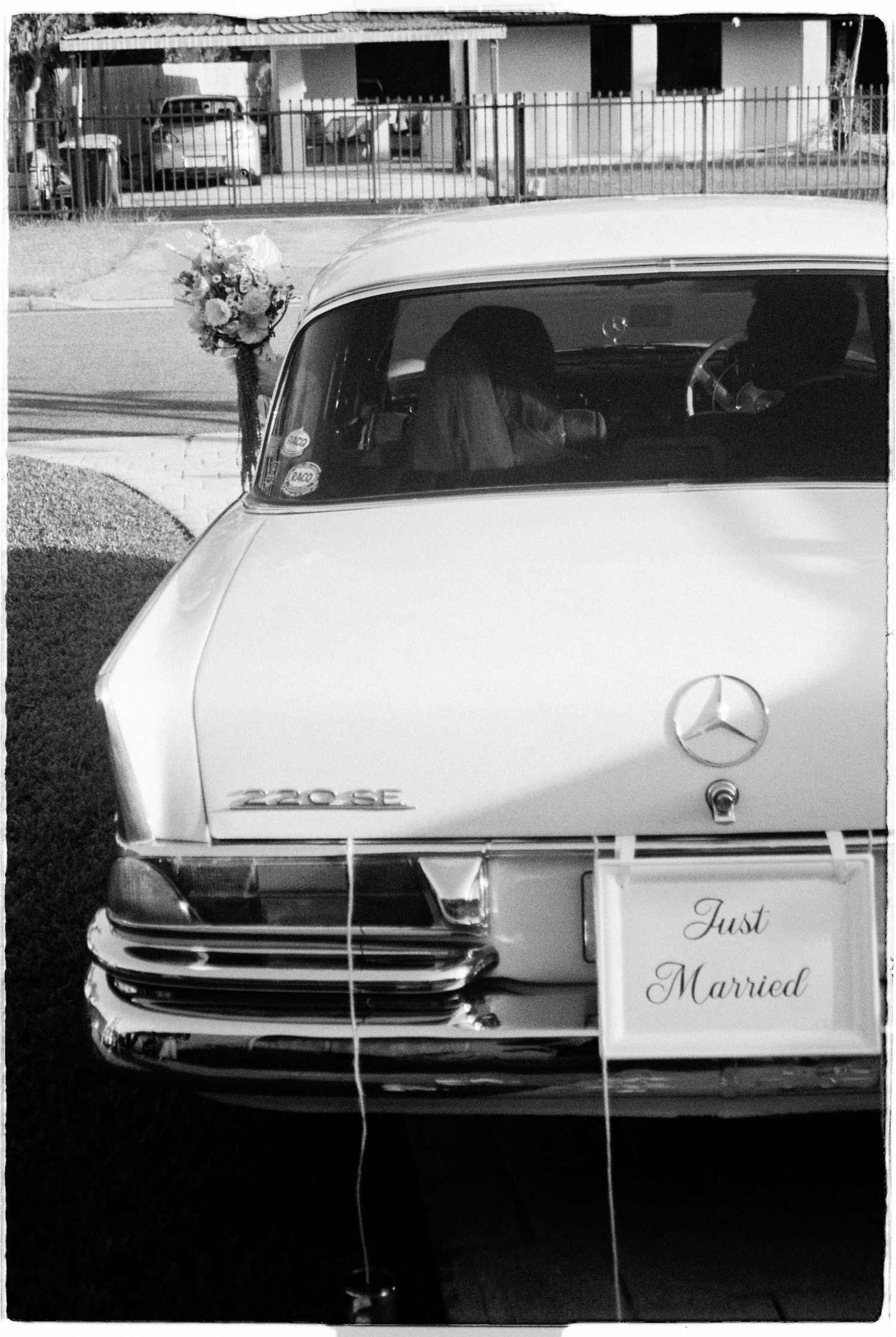 Vintage white Mercedes-Benz 220SE with Just Married sign and floral bouquet on trunk.