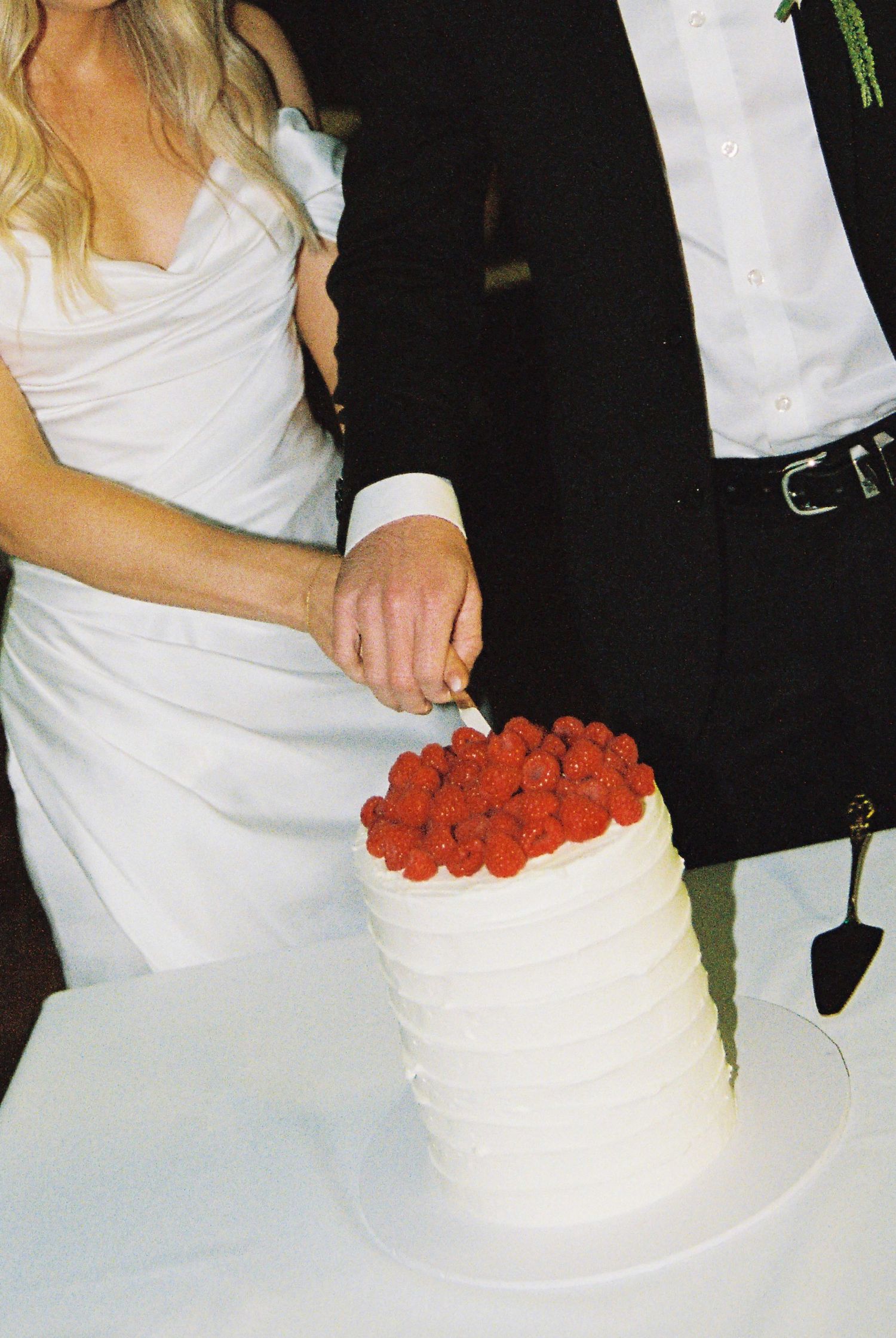 Bride and groom cutting white wedding cake topped with fresh raspberries at wedding reception.