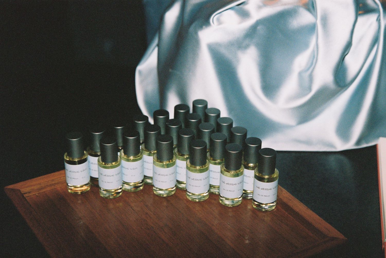 Rows of small perfume oil bottles displayed on wooden tray as wedding favors for guests.