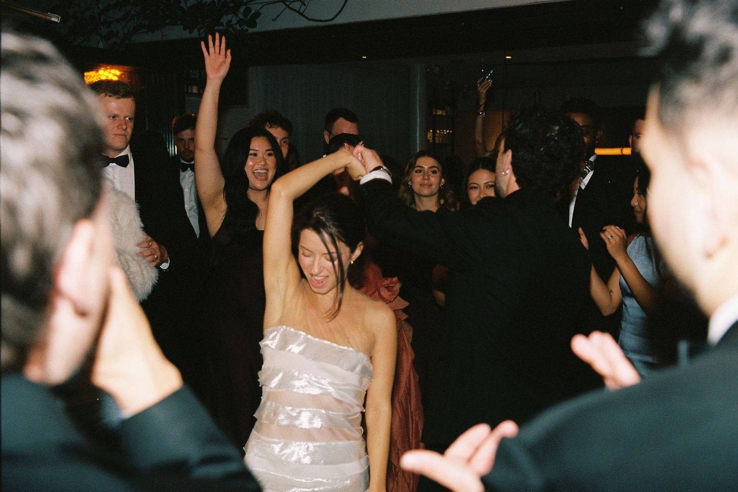 Bride dancing joyfully with guests on crowded wedding reception dance floor.