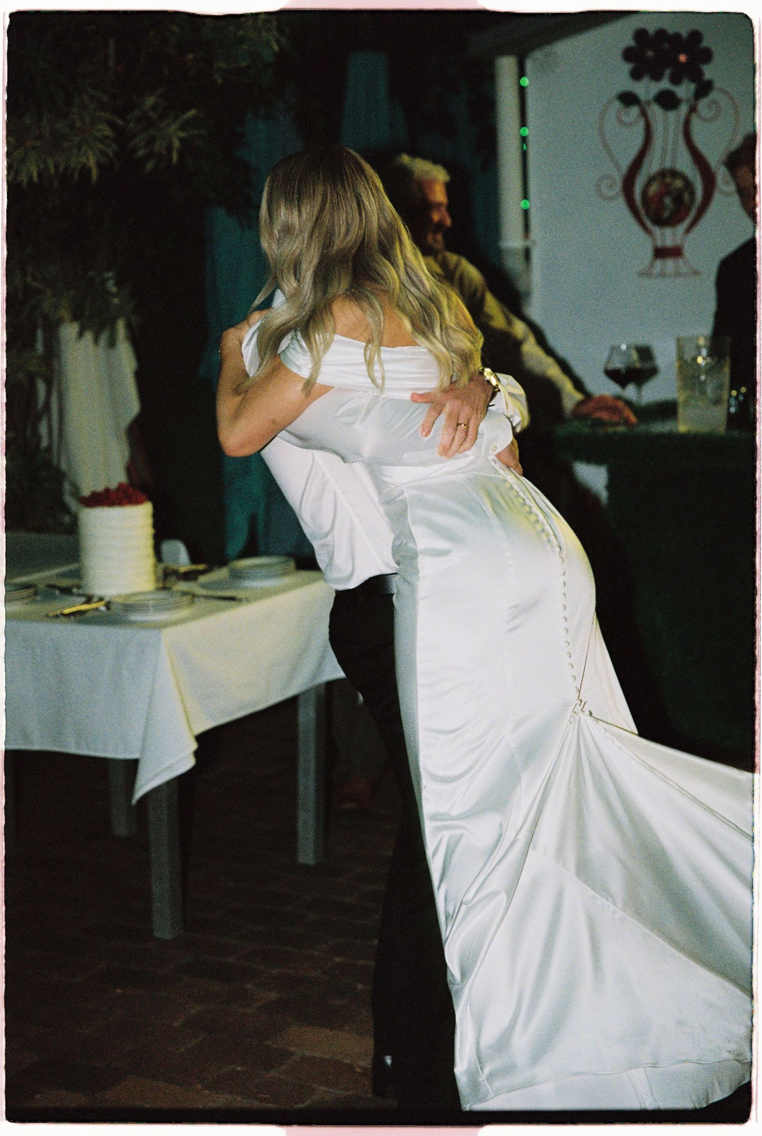 Bride and groom share their first dance, her elegant white gown with button train on display.