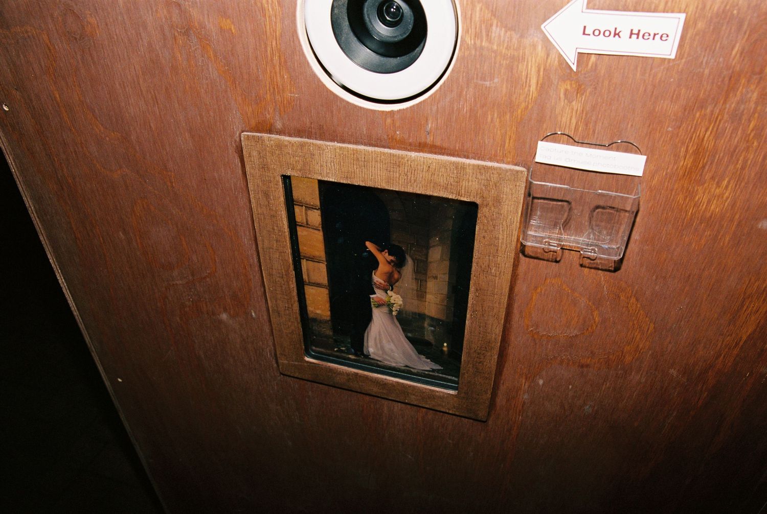 Vintage photo booth with a small viewing window showing a bride in a white wedding dress inside.