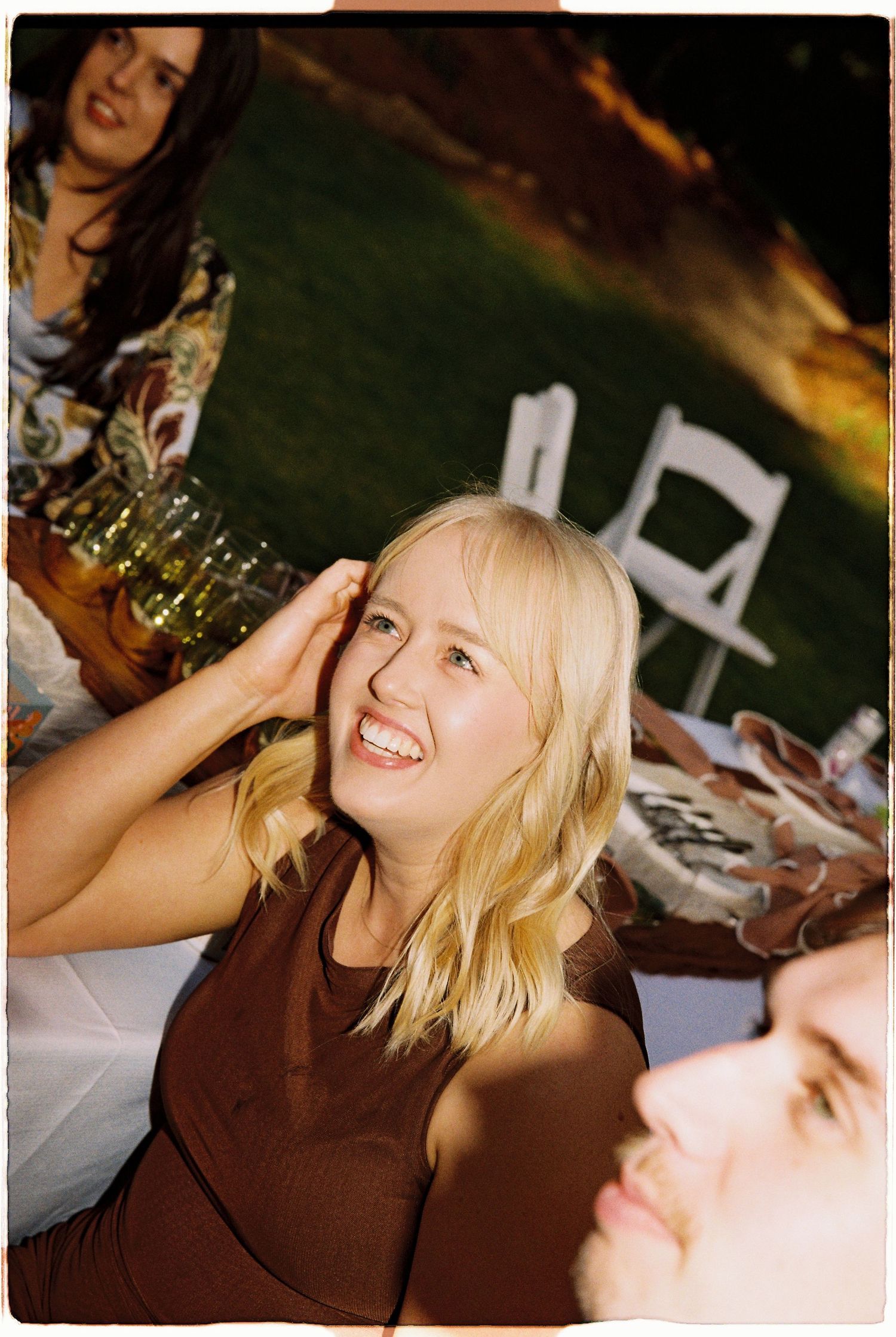 Smiling blonde woman in brown dress enjoying outdoor evening wedding reception.