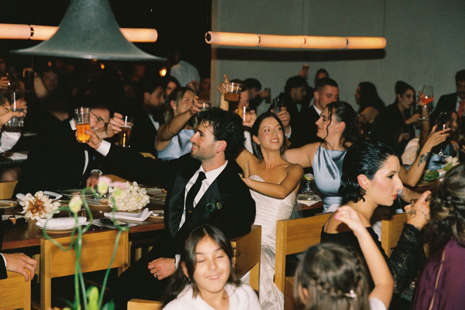 Wedding guests raising glasses in a toast during candlelit reception dinner celebration.