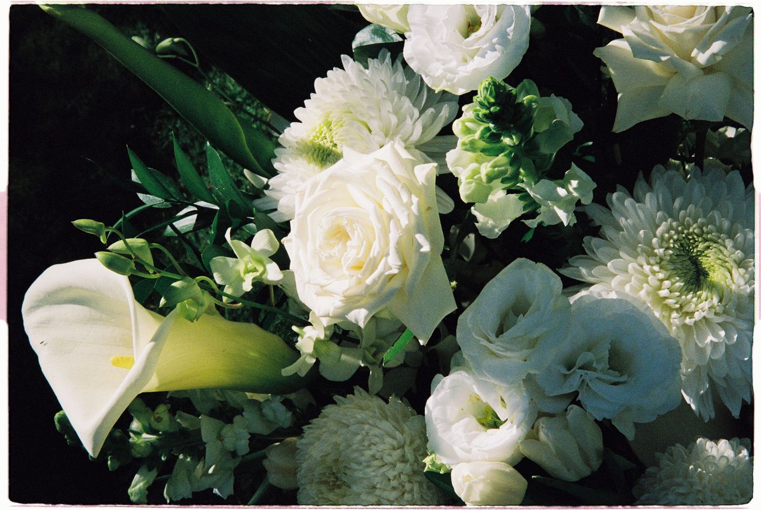 Close-up of elegant white wedding bouquet featuring calla lilies, roses, chrysanthemums, and lisianthus.