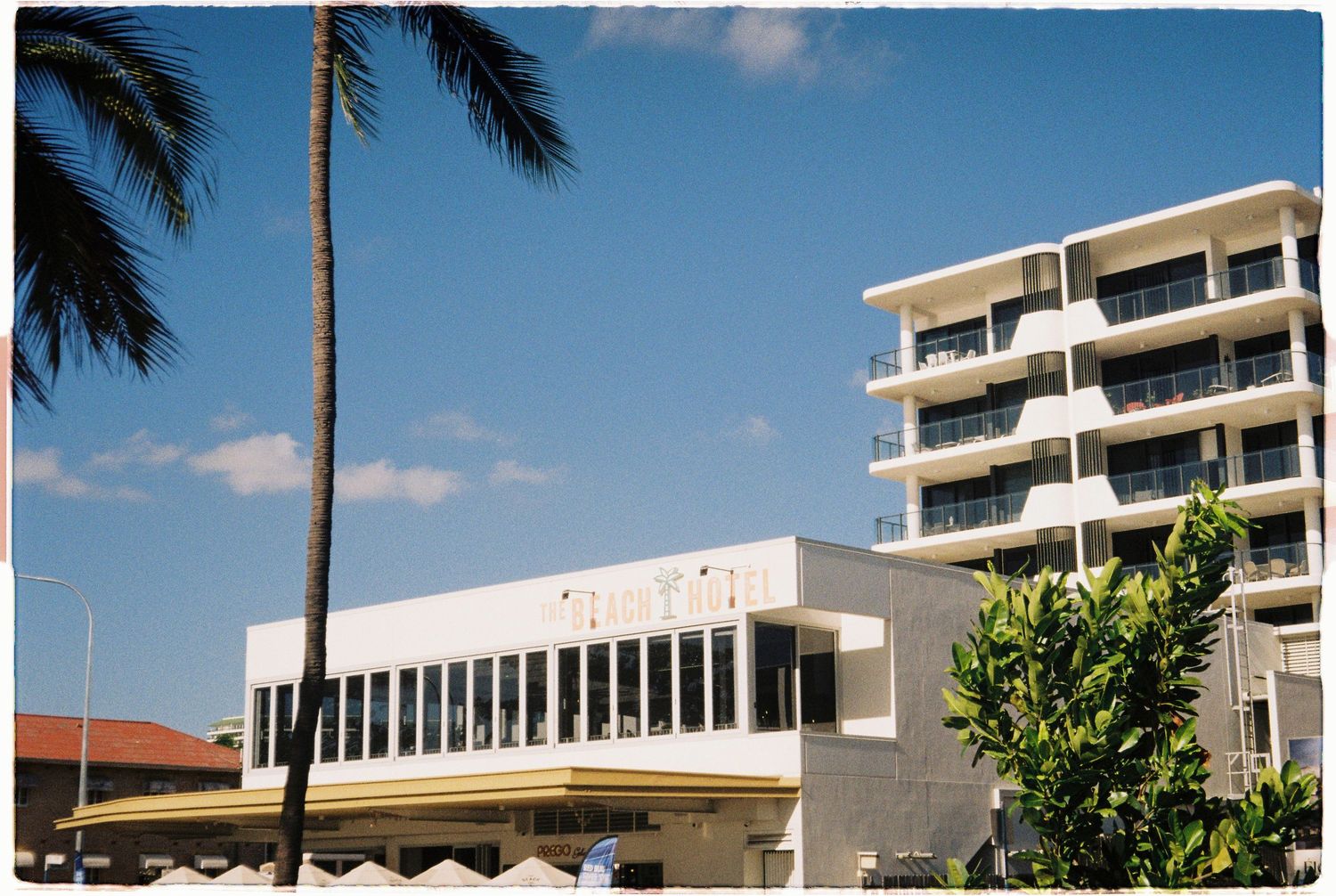 Modern white commercial building beside a multi-story apartment block under a bright blue sky.