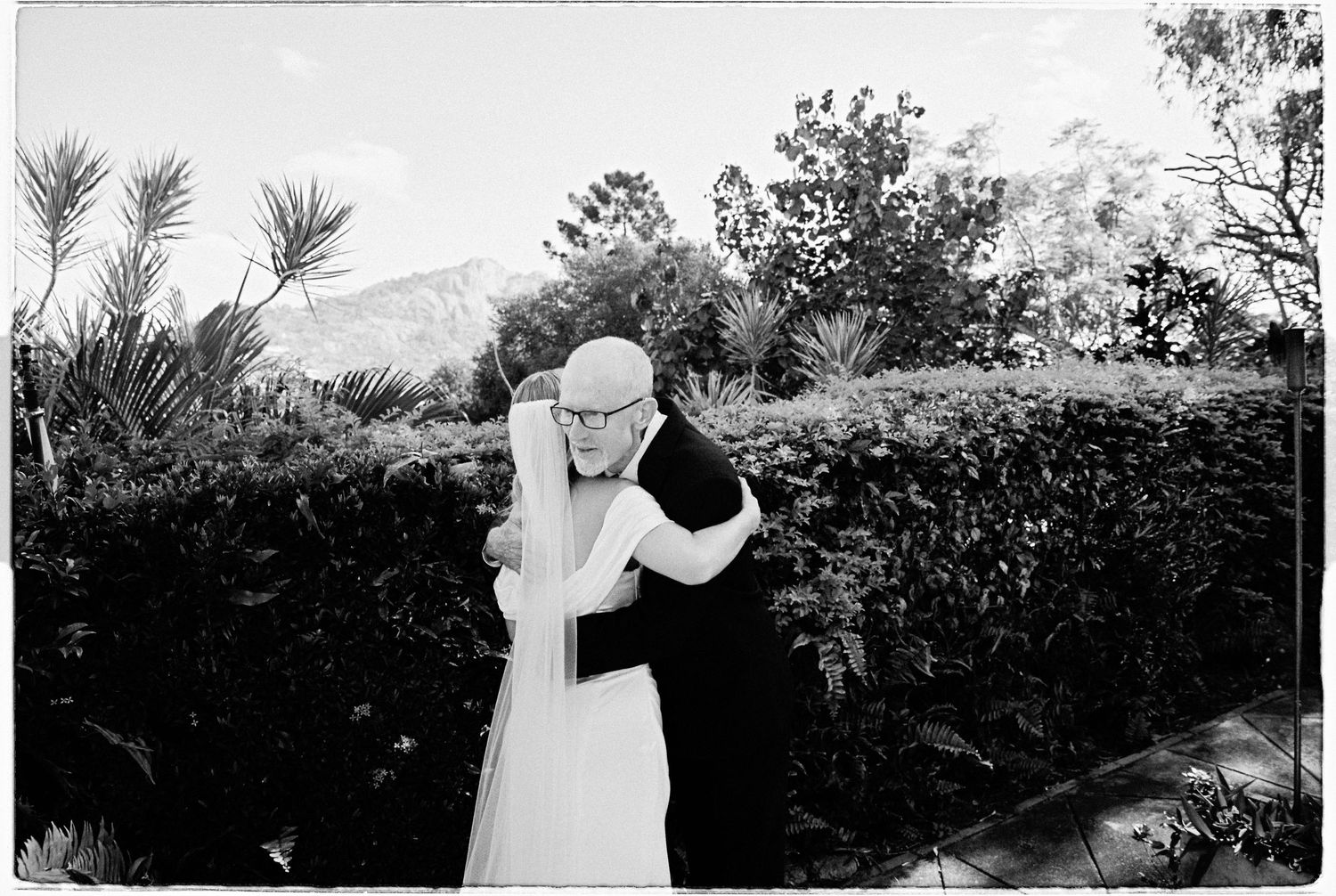 Bride and groom share a romantic embrace in a lush garden setting on their wedding day.