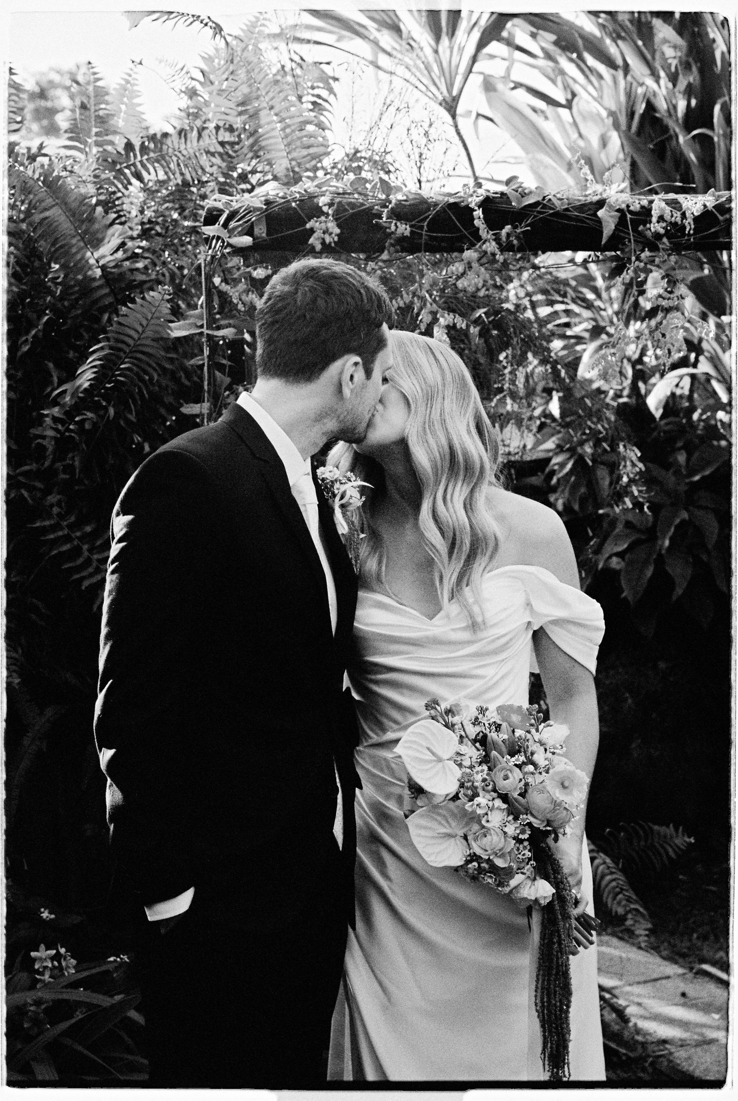 Bride and groom sharing a romantic kiss in a lush garden, black and white wedding photo.