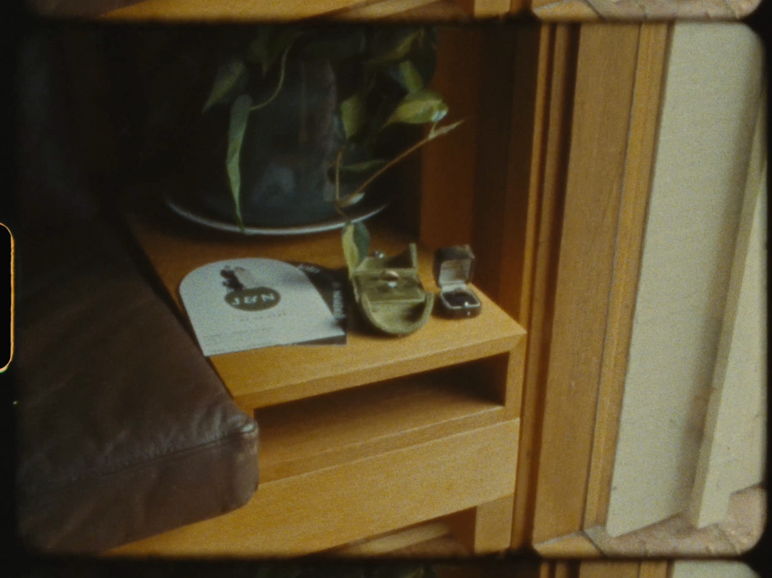 A wooden bedside table with a plant, glass, and magazine in a cozy interior setting.