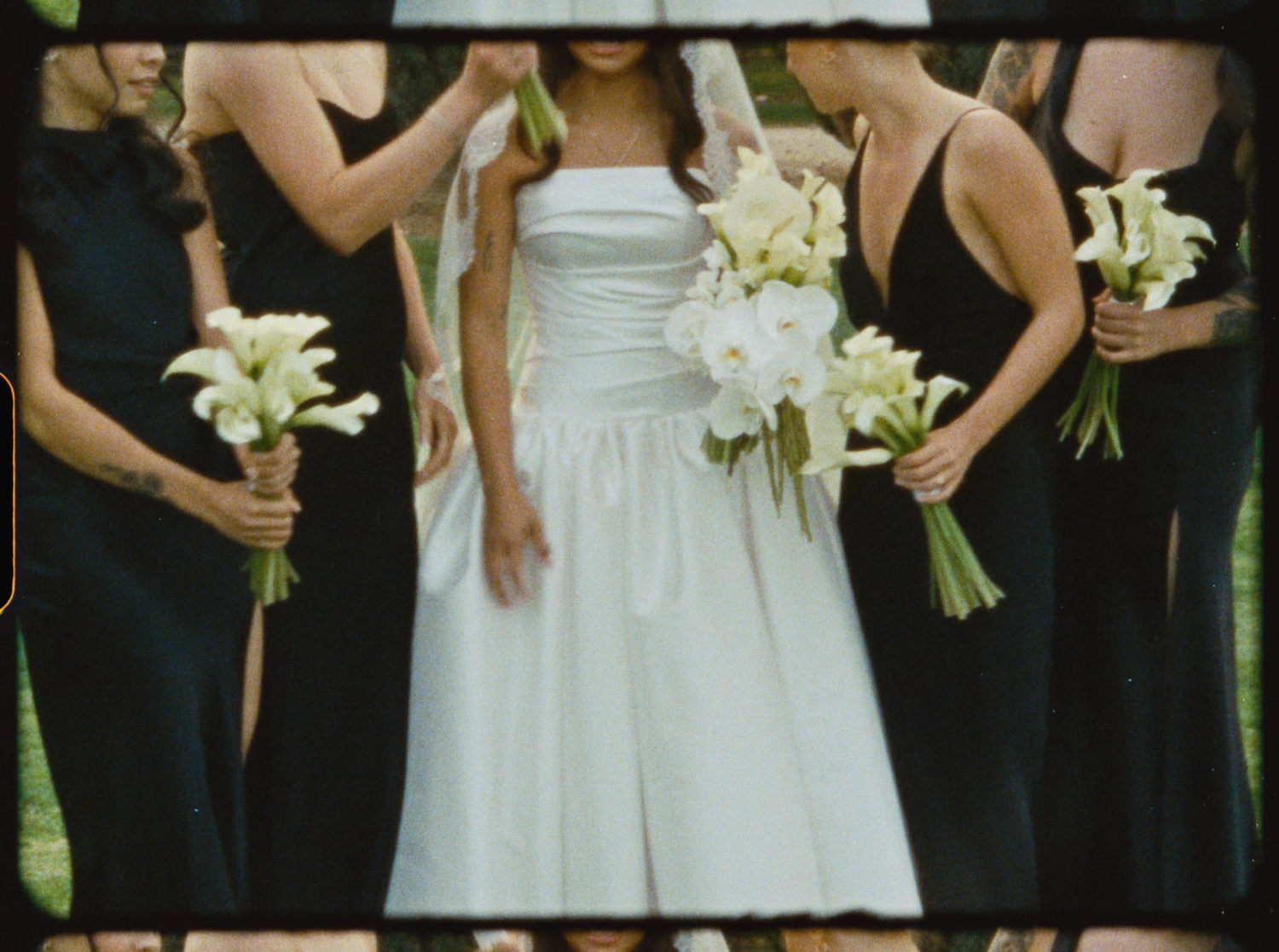Bride in white dress holding bouquet surrounded by bridesmaids in black dresses with white calla lily bouquets.