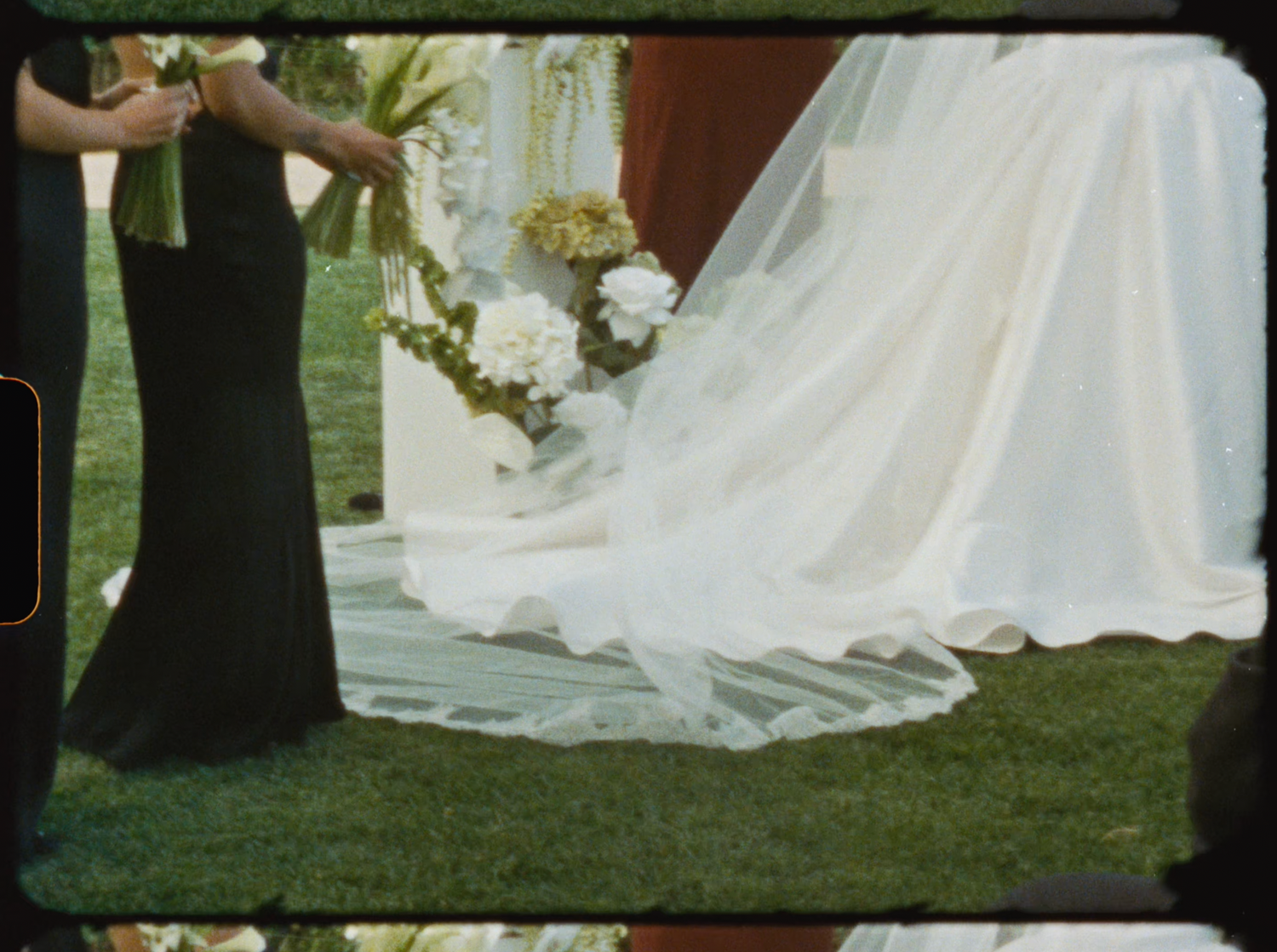 Close-up of brides flowing white veil and gown train at outdoor wedding ceremony.