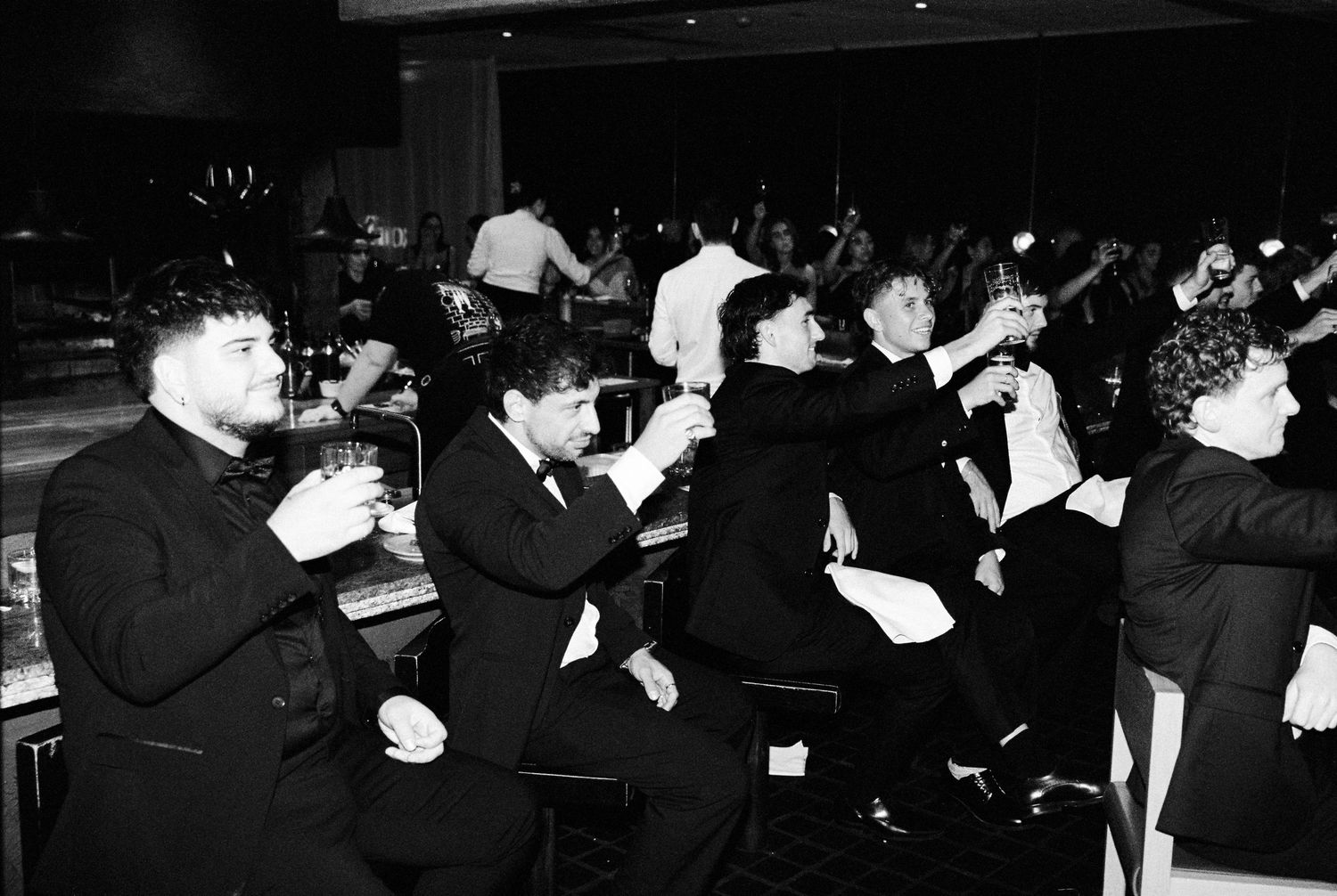 Groomsmen in tuxedos raising glasses in a celebratory toast at wedding reception.