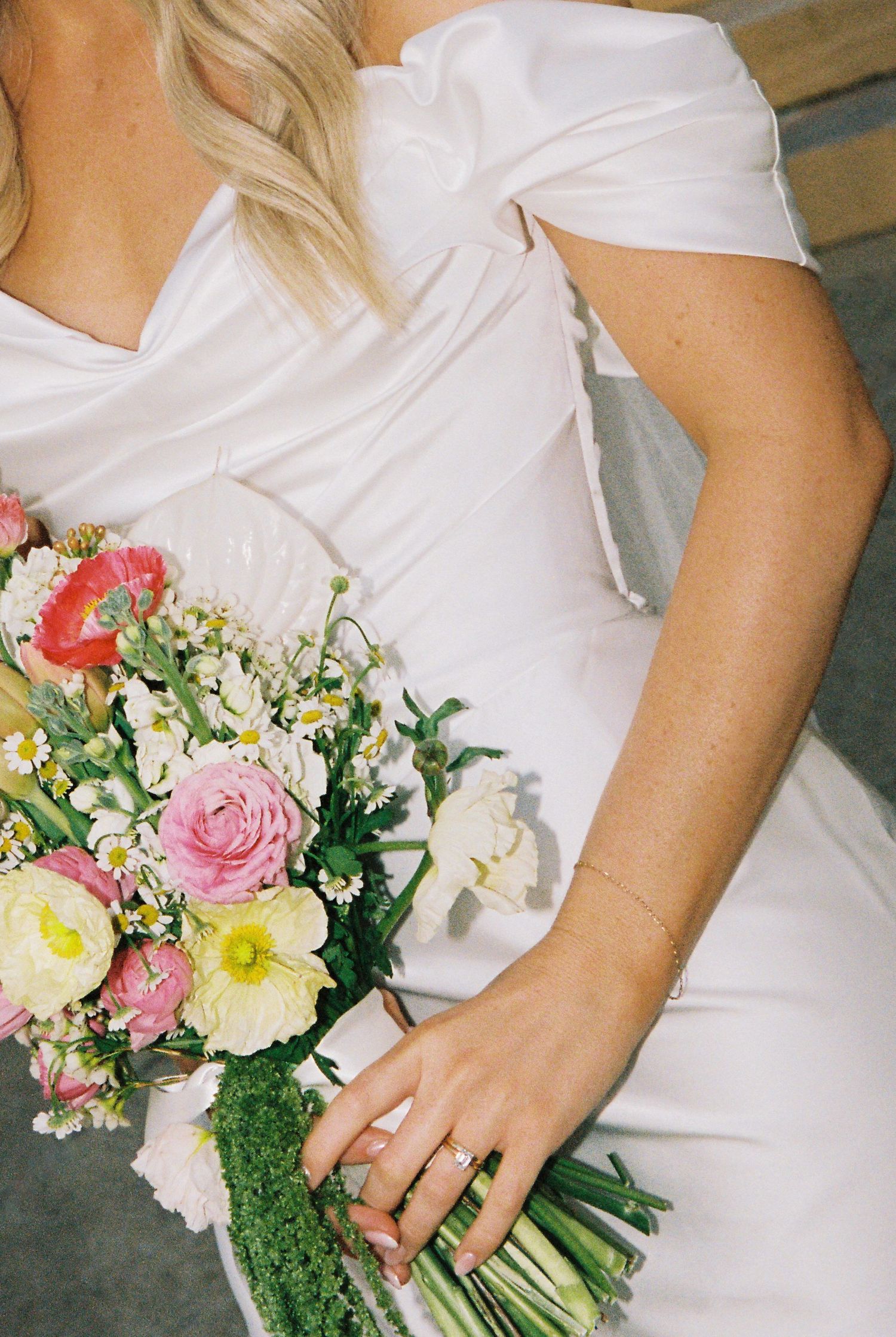 Bride in off-shoulder white gown holding pink and yellow floral wedding bouquet.