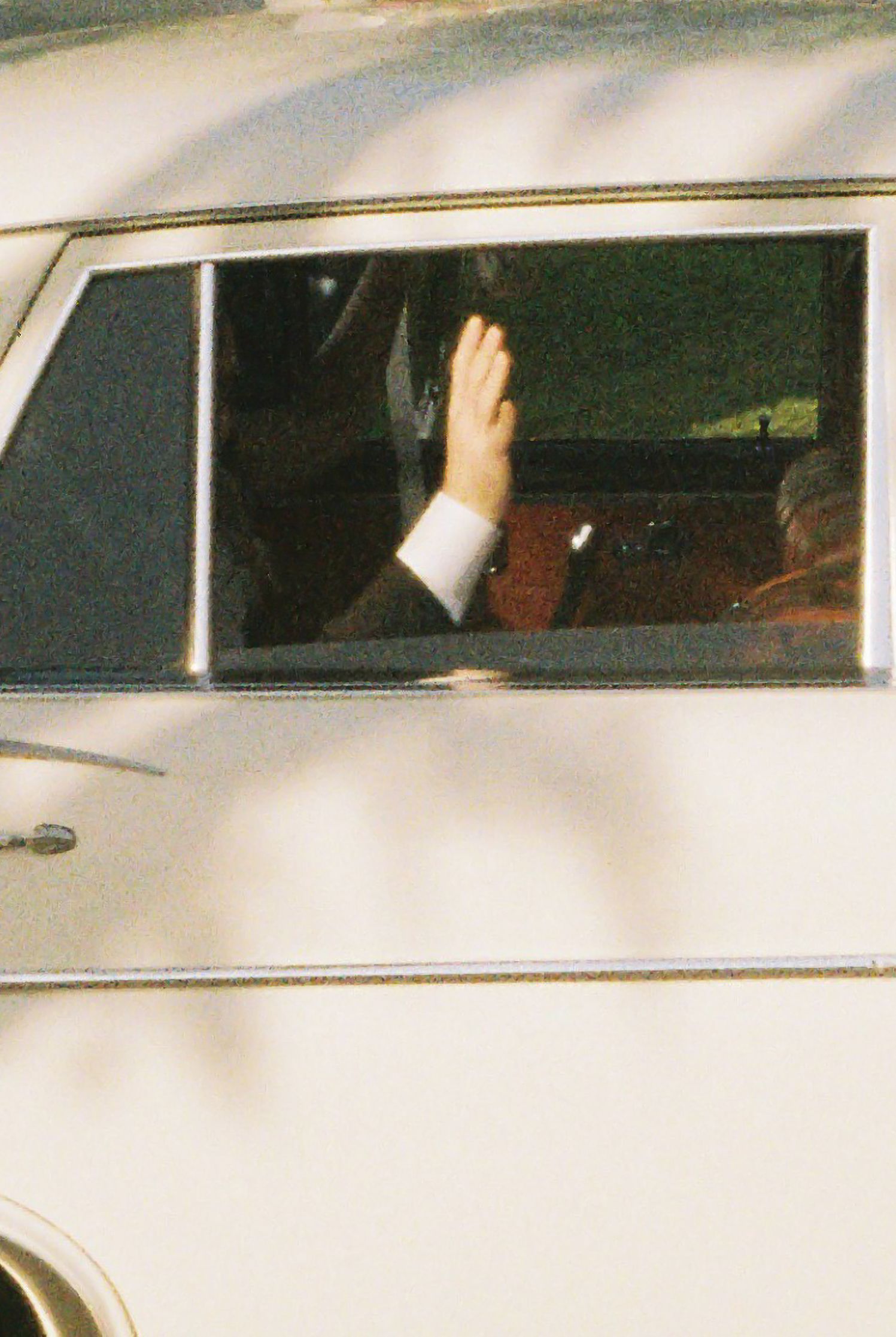A person waving from inside a cream-colored vintage vehicle through an open car window.