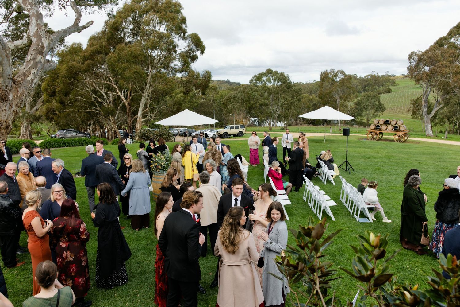 Guests mingle on lush green lawn at elegant outdoor wedding ceremony with white chairs and marquee tents.