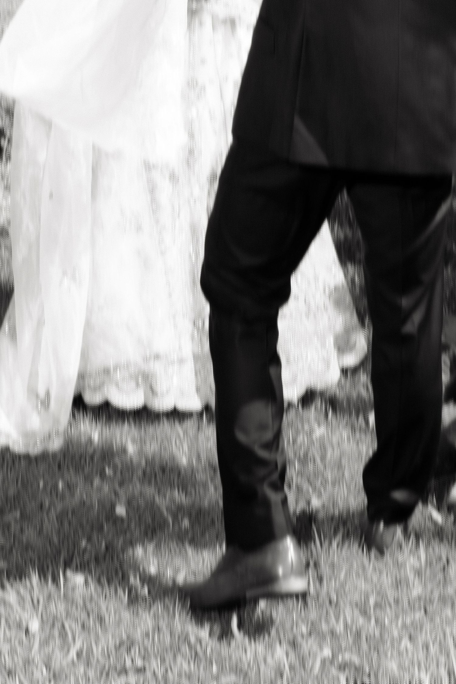 Black and white blurred motion shot of bride and groom walking on grass together.