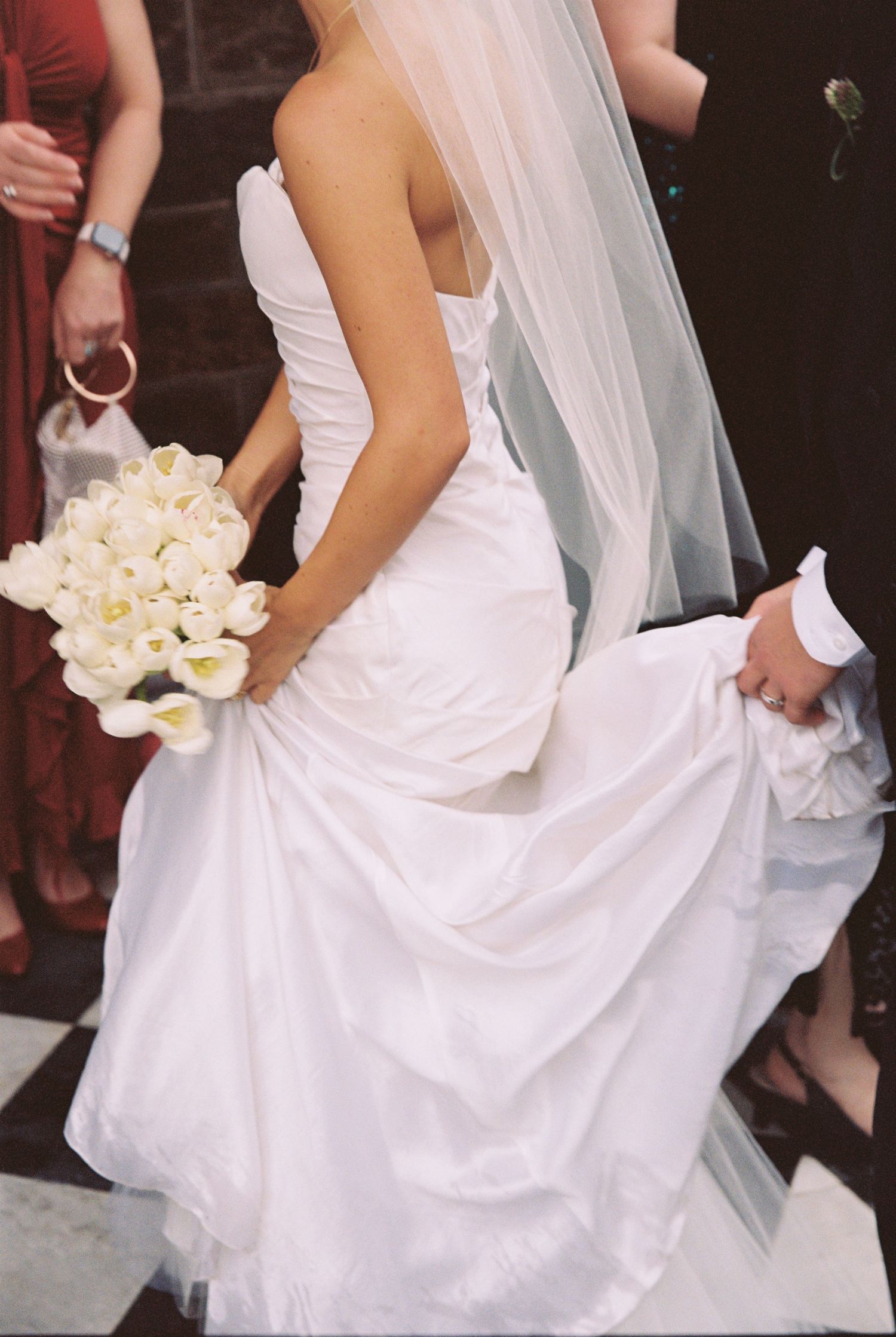 Bride in strapless white wedding gown holding white calla lily bouquet with veil flowing behind her.