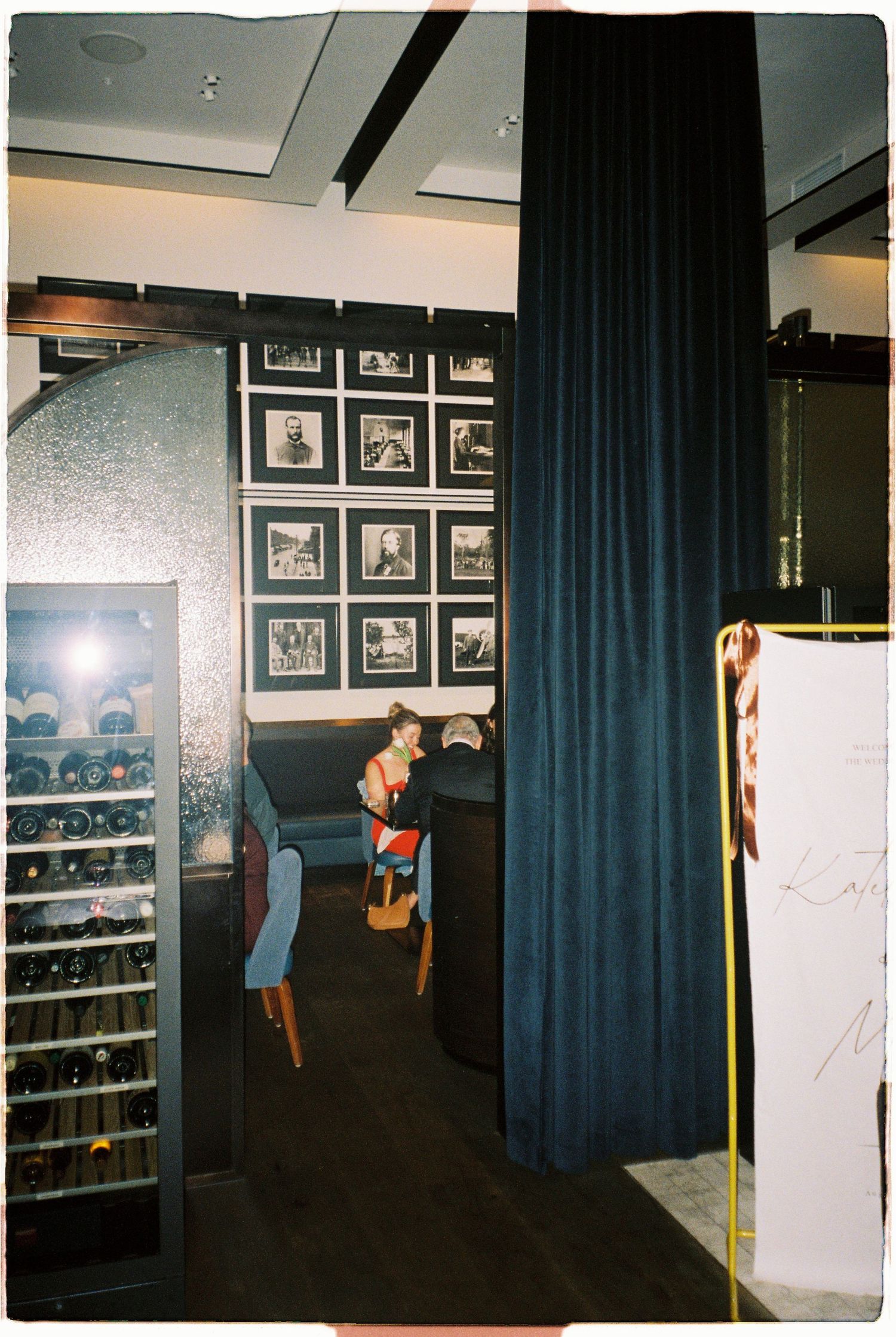 Elegant restaurant interior with wine fridge, navy curtains, and black and white framed photos.