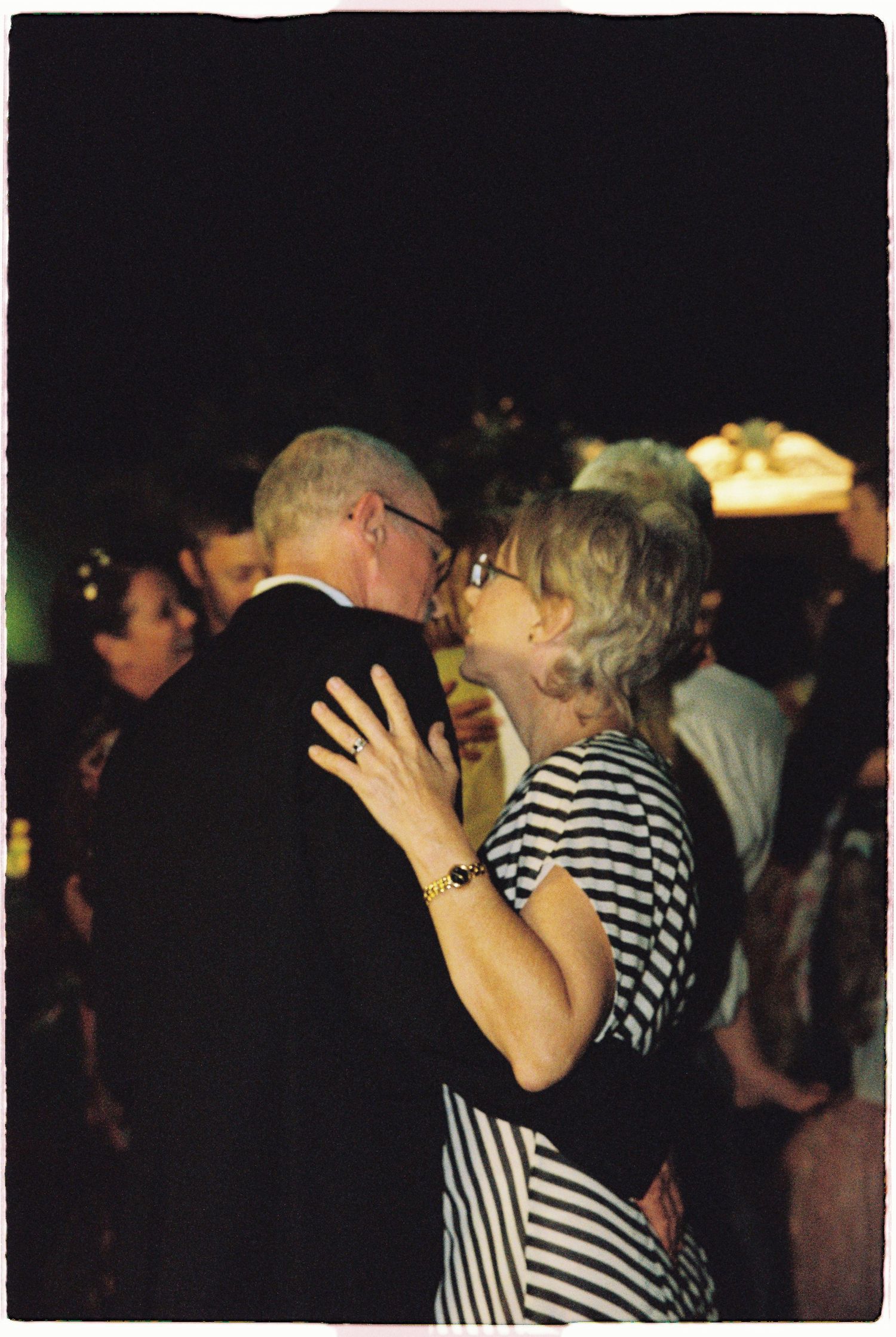 Couple sharing a romantic kiss on the dance floor at a wedding reception in dim evening lighting.