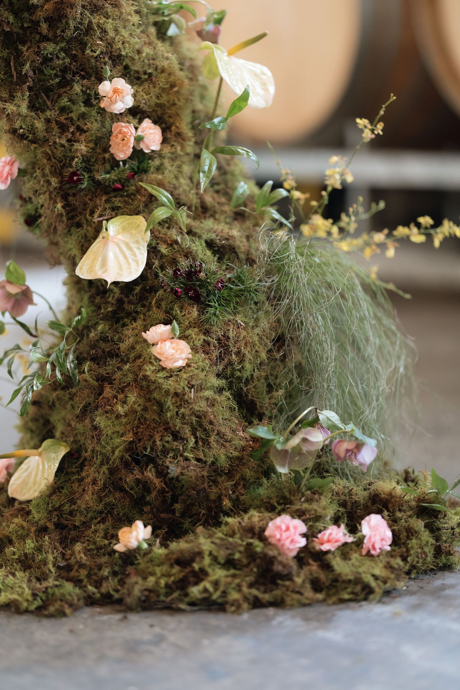 Elegant wedding floral arrangement featuring moss, pink carnations, and white anthurium flowers.