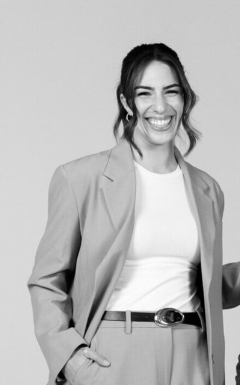 Smiling woman in blazer and white tee poses confidently in black and white professional portrait photo.